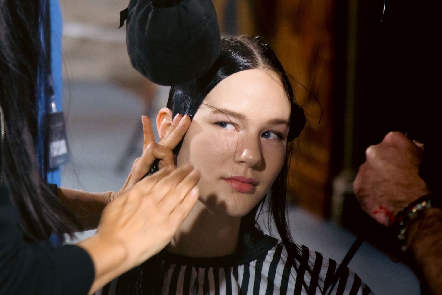 Makeup artist applying foundation to a young model backstage at a fashion show.
