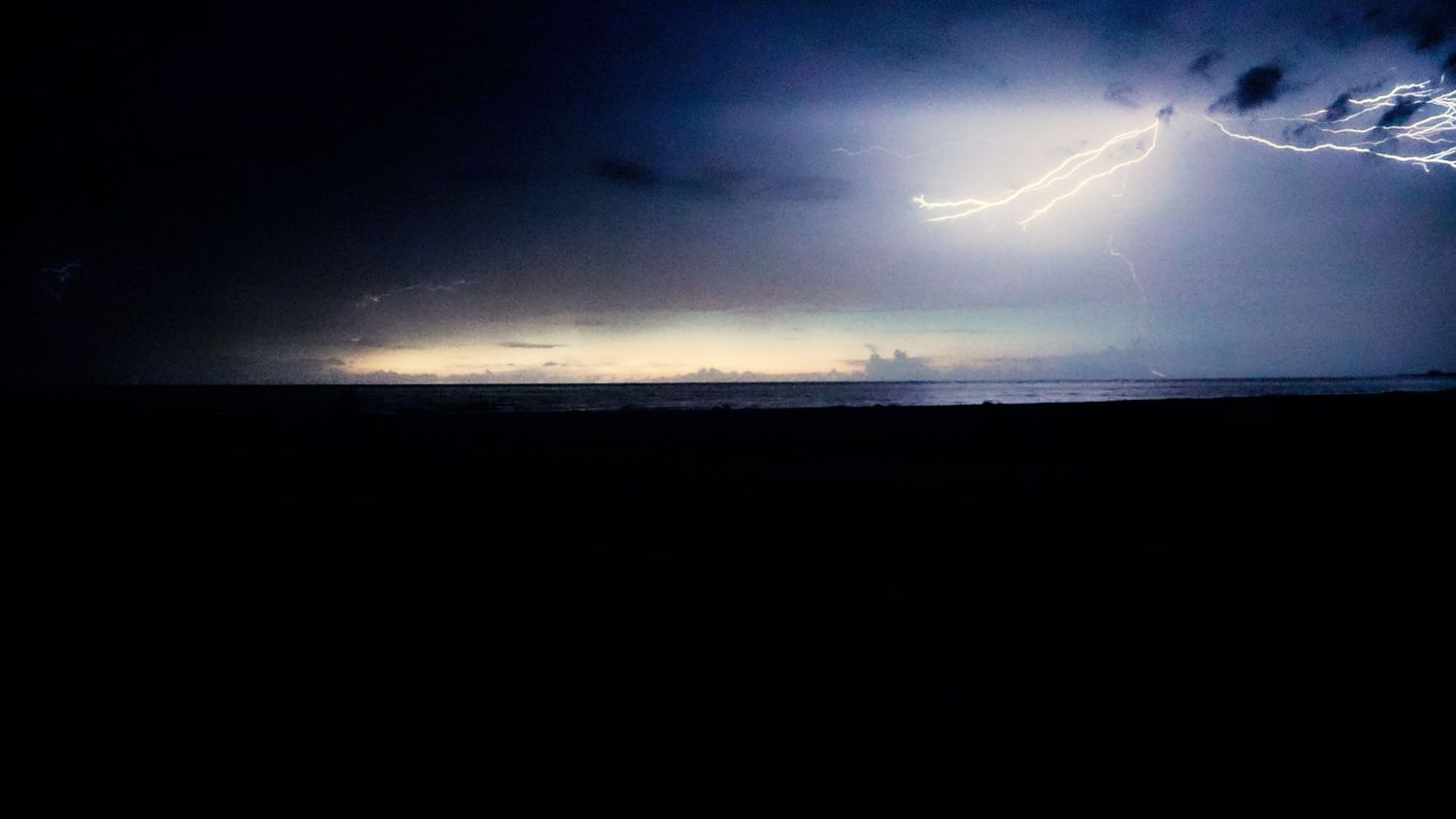 Dramatic lightning strike over dark ocean horizon at night with stormy clouds.