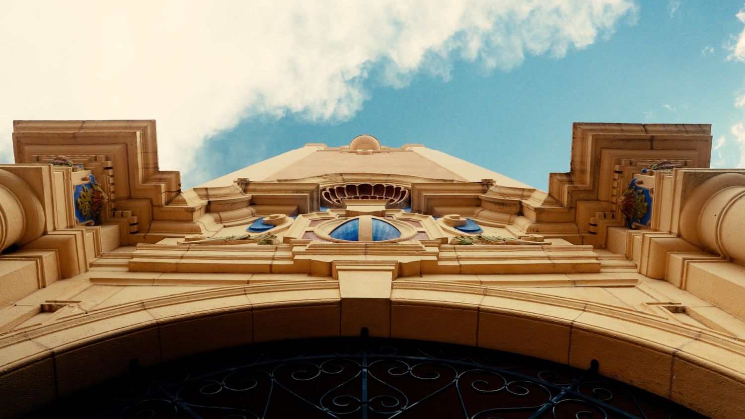 Low angle view of ornate Art Deco building facade with golden details against blue sky with clouds.