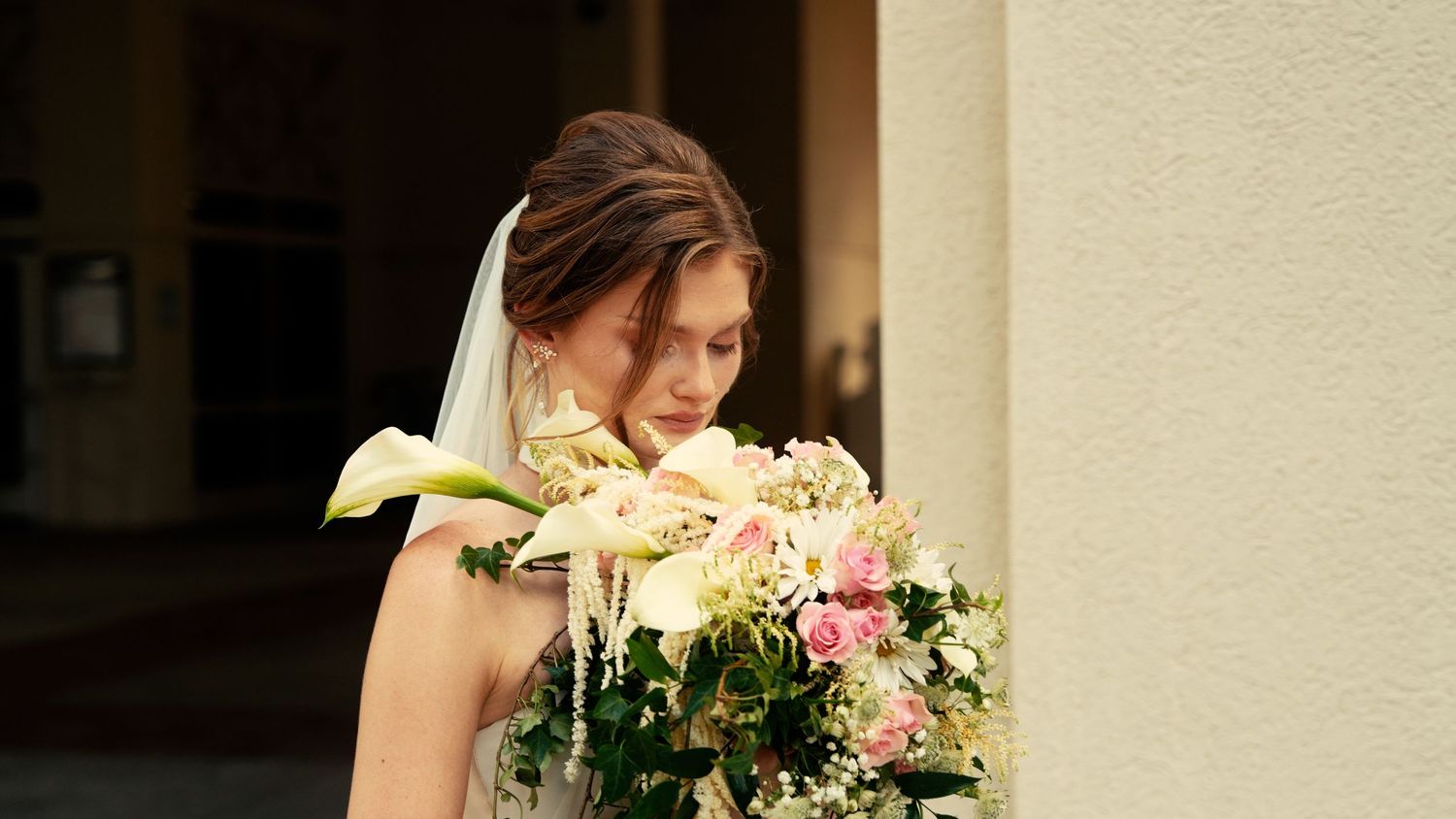 Bride in white wedding dress and veil holding beautiful bouquet of pink roses and calla lilies.