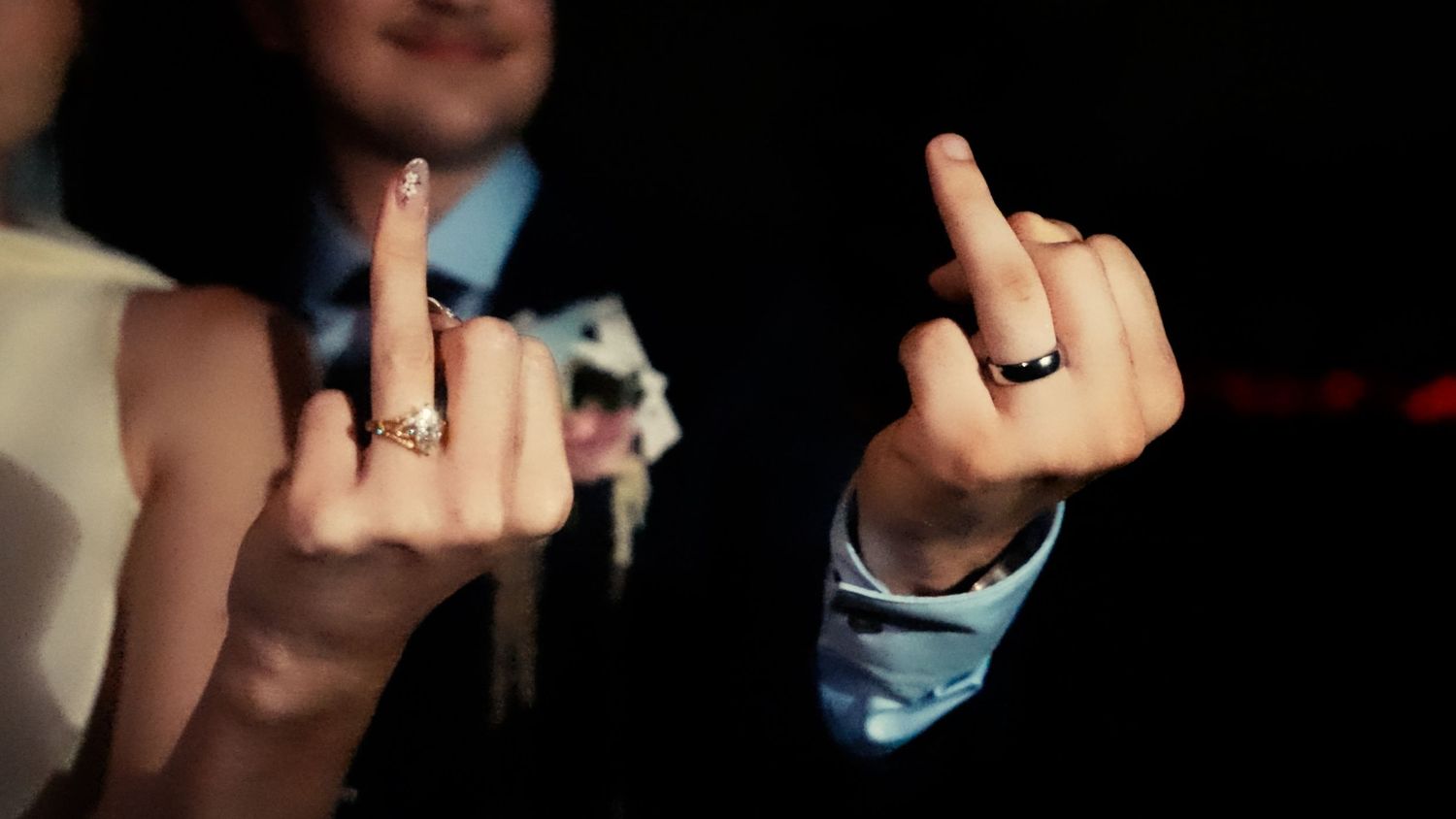 Bride and groom displaying wedding rings on fingers in dark romantic setting.