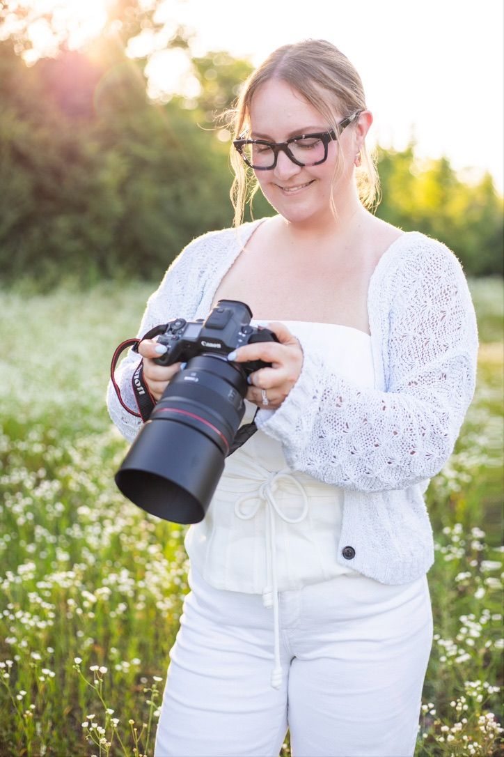 Dayton Ohio area photographer checks her camera monitor and smiles. She is standing in a wildflower field and the sun is glowing behind her.