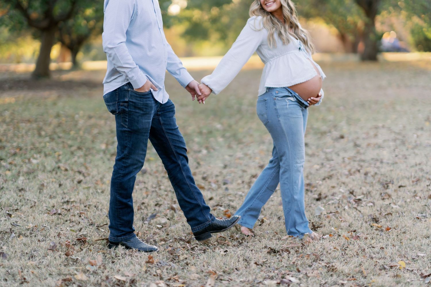 Pregnant couple holding hands and walking through a scenic outdoor area during a maternity photoshoot.