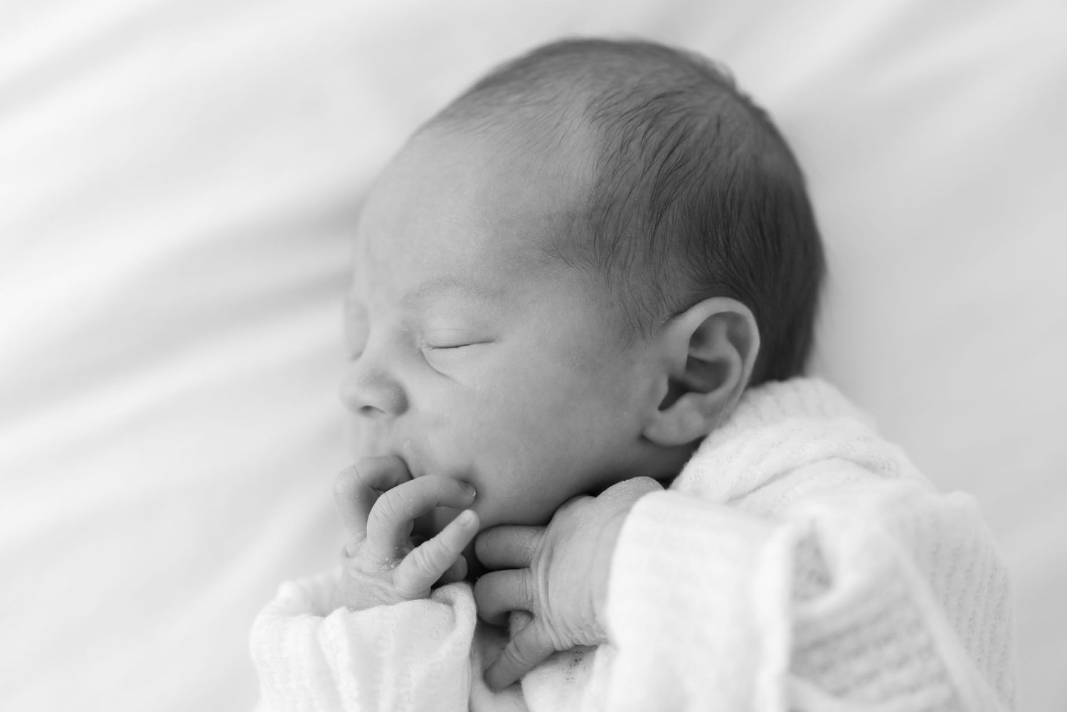 Peaceful sleeping newborn baby in black and white photo with hands tucked under chin.