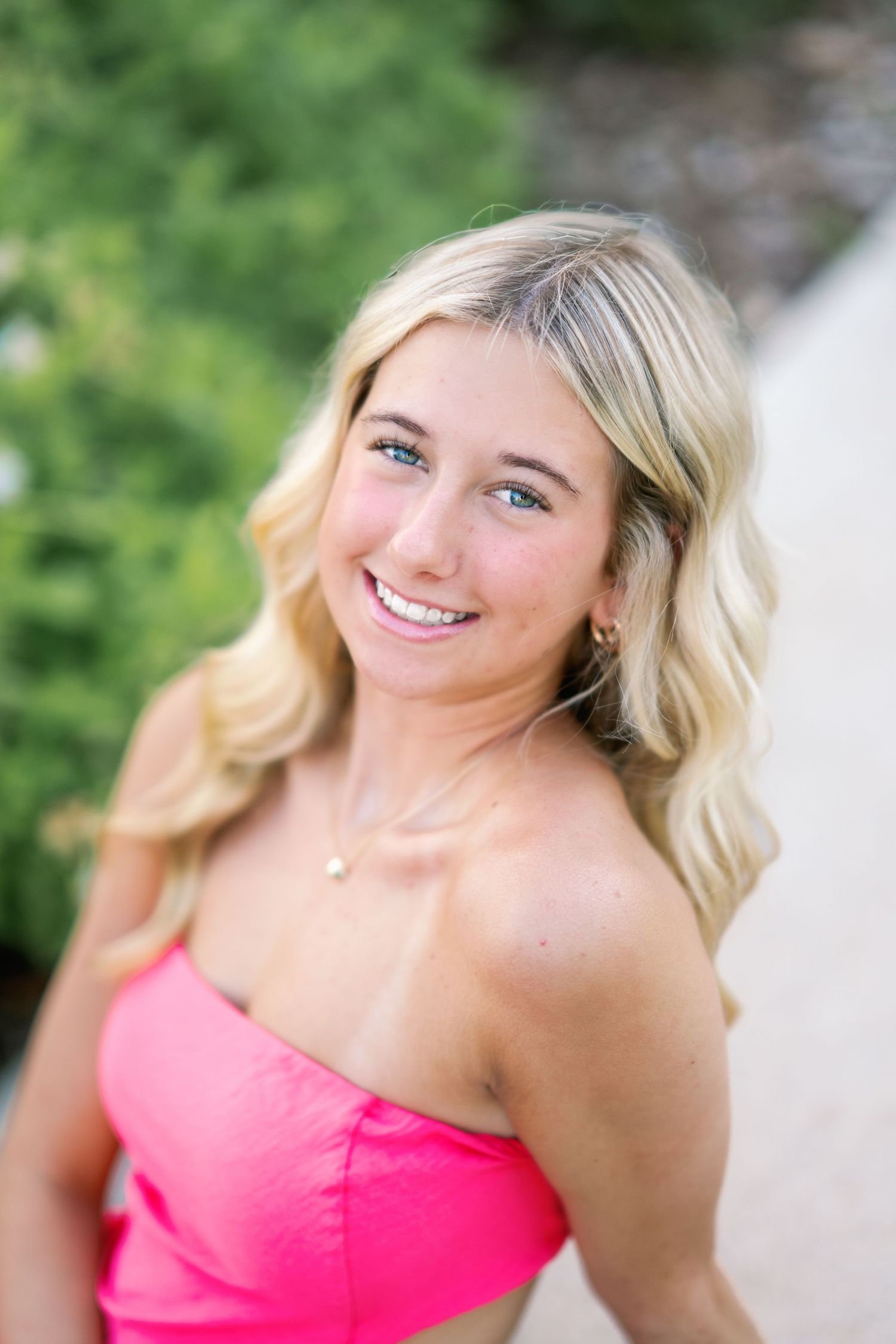 Smiling blonde teenage girl in pink crop top posing outdoors for senior portrait photos.