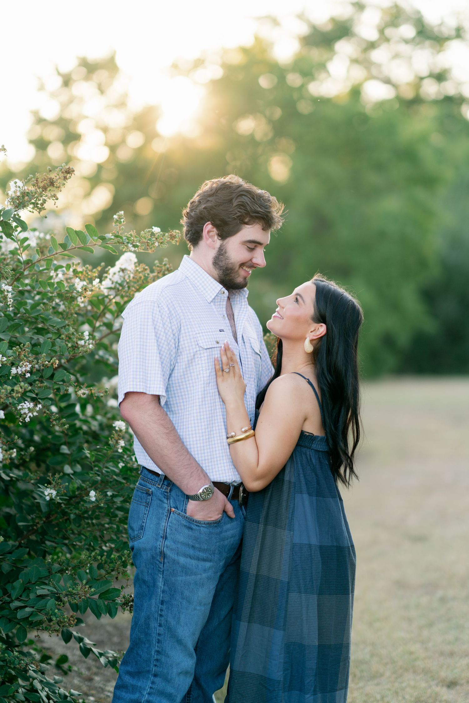 Couple sharing romantic moment at golden hour near blooming bushes in outdoor setting.