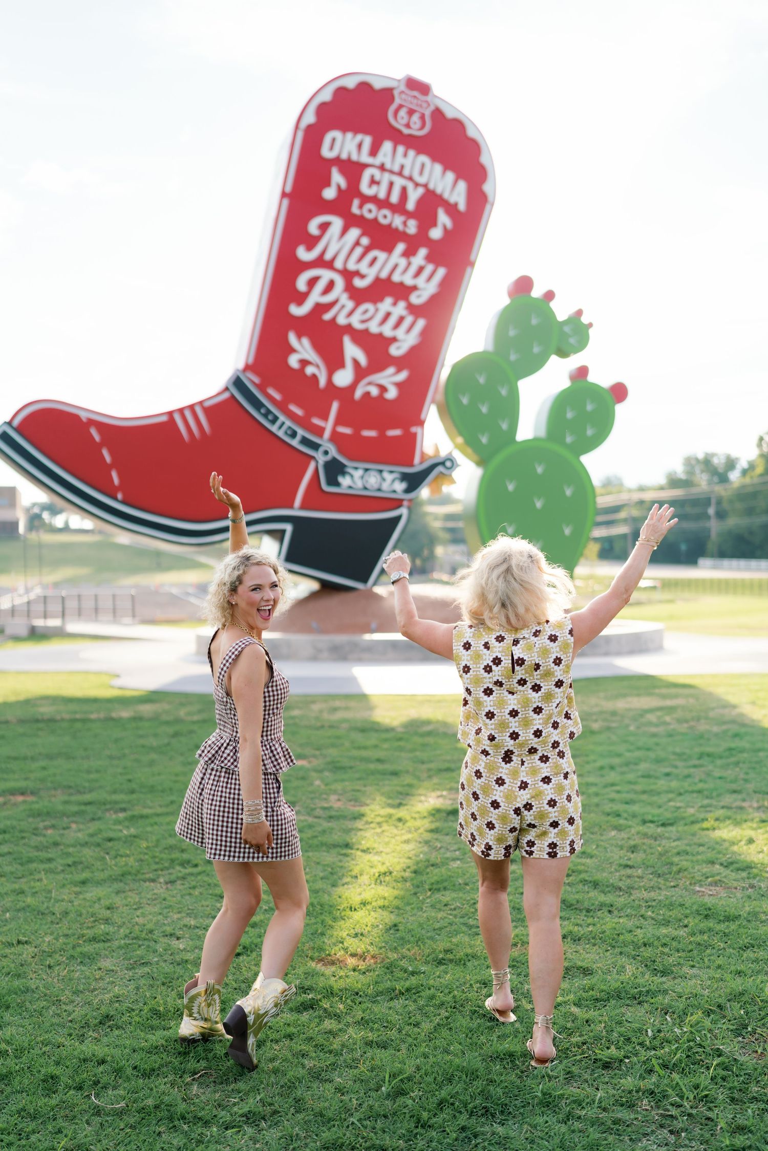 Two women dancing in front of Oklahoma City Route 66 Mighty Pretty boot and cactus sign.