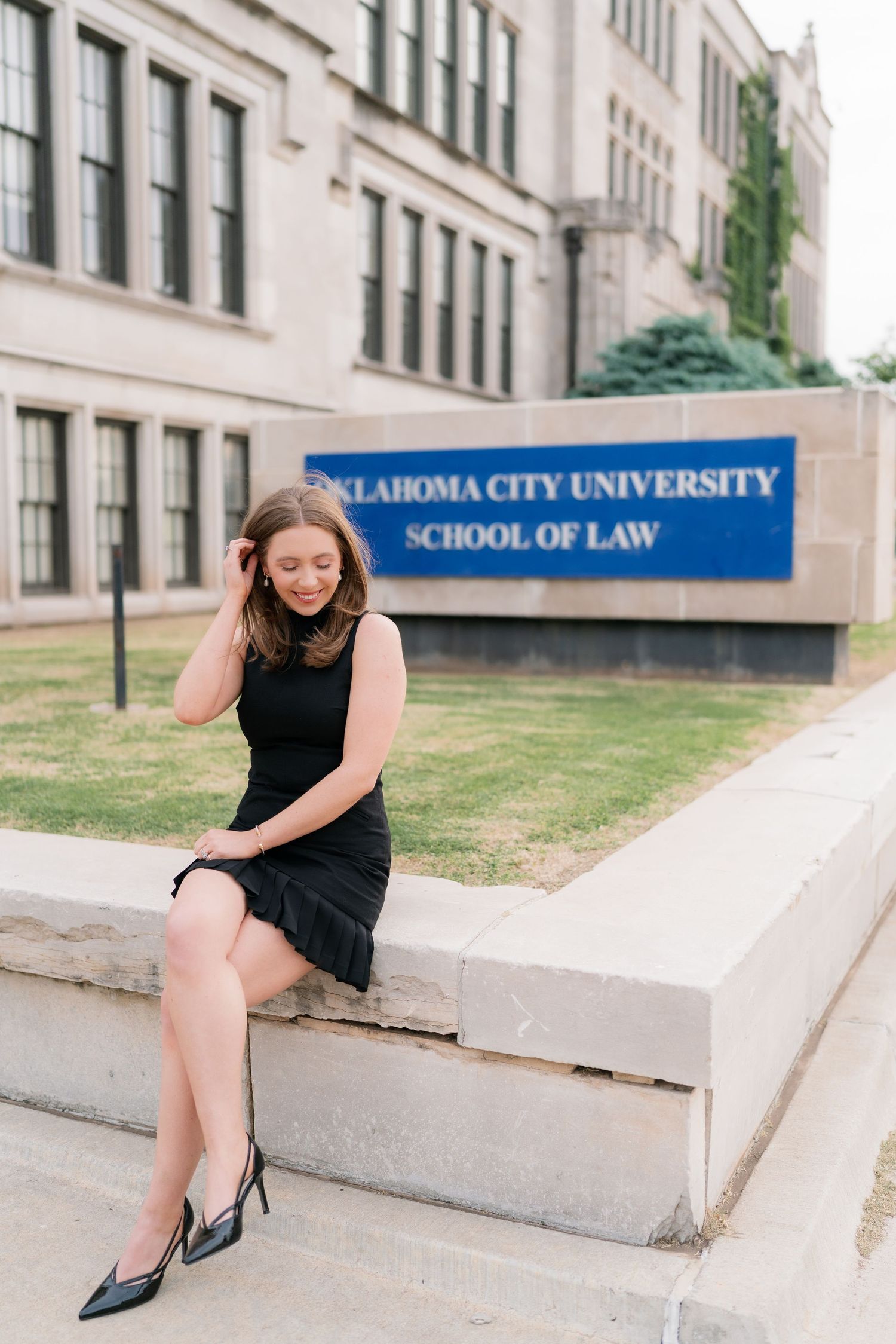 Woman in black dress sitting outside Oklahoma City University School of Law building.