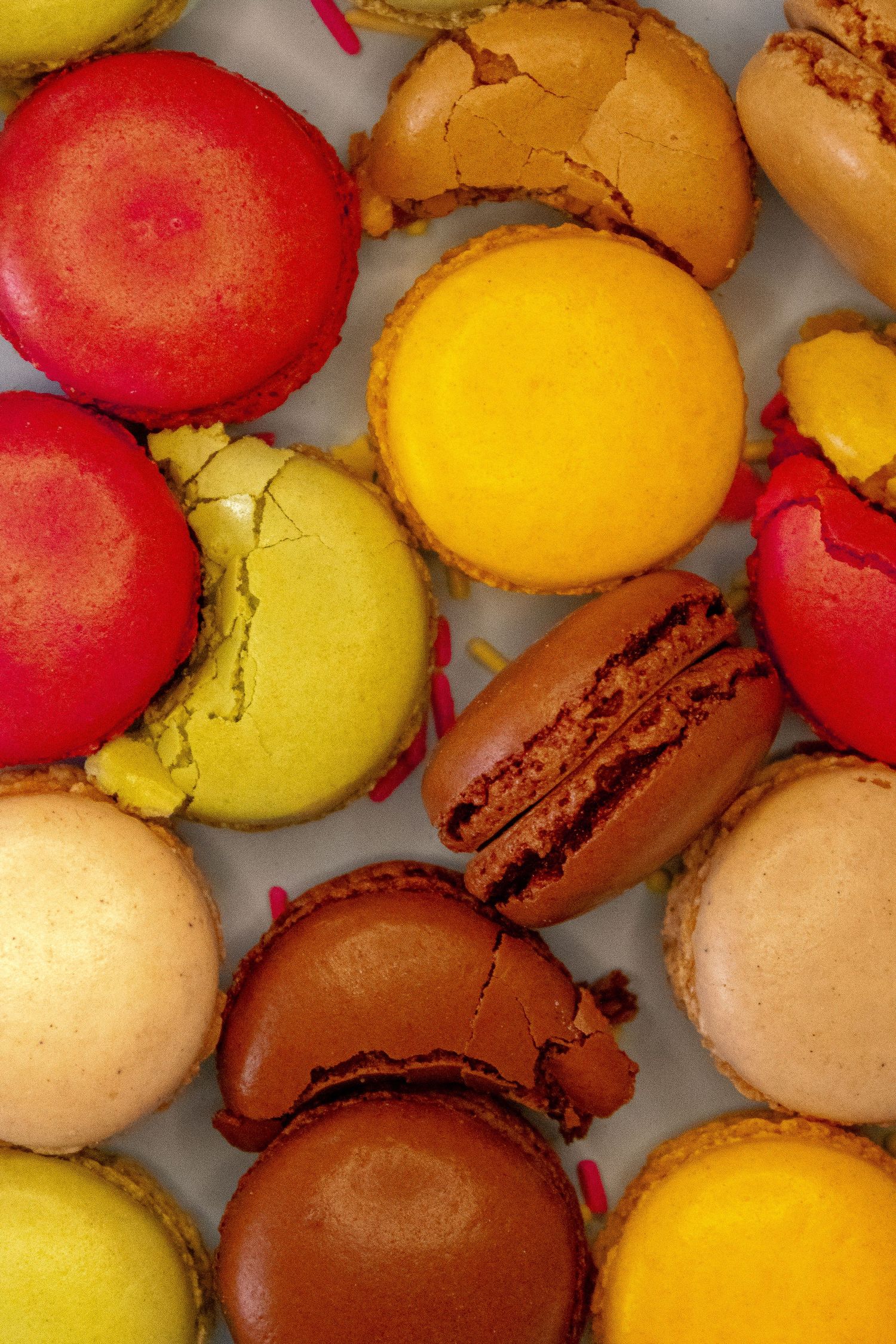 Assorted colorful French macarons in red, yellow, green, and brown scattered on white surface.