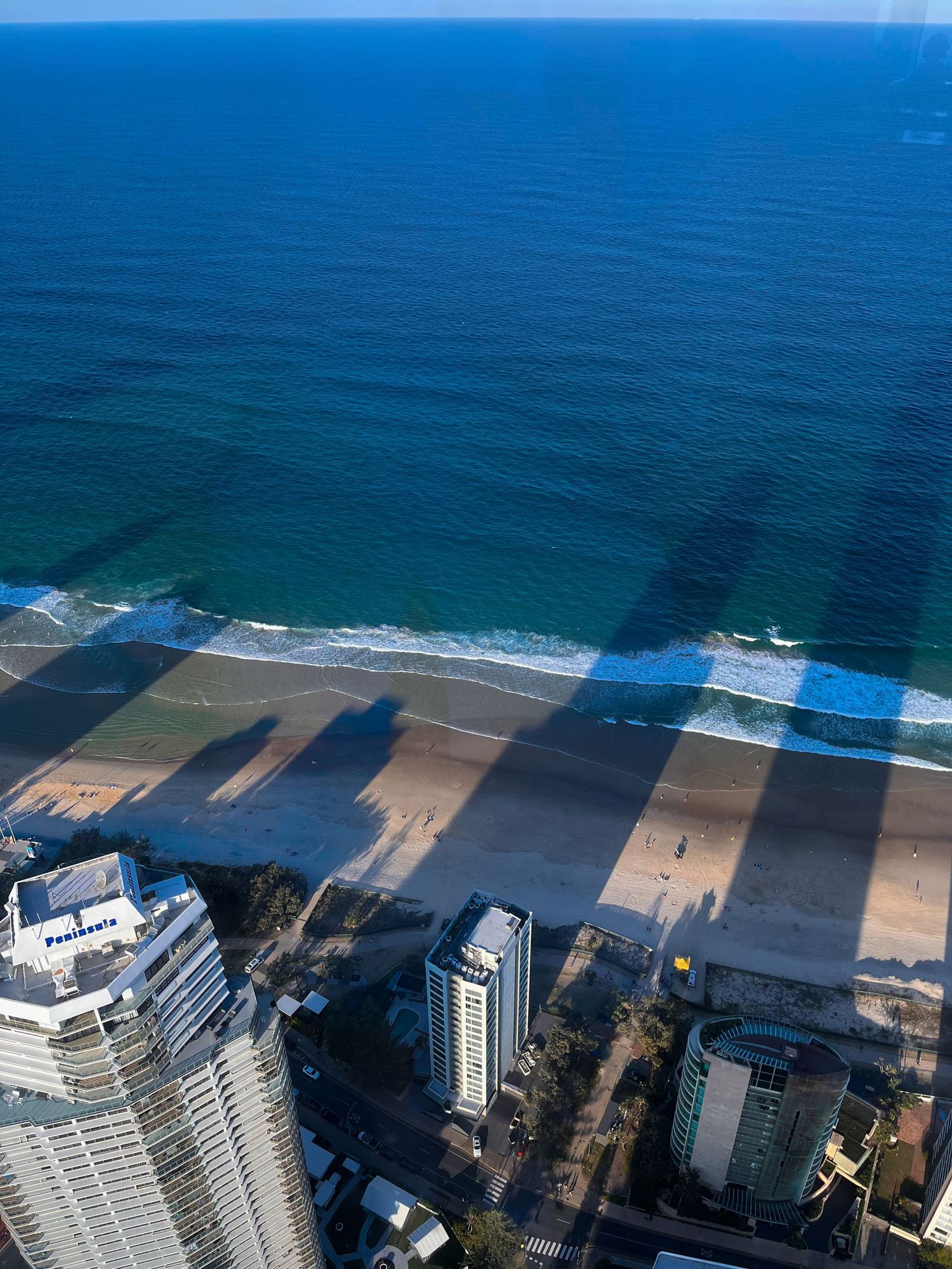 Aerial view of Surfers Paradise beach with skyscraper shadows cast over golden sand.