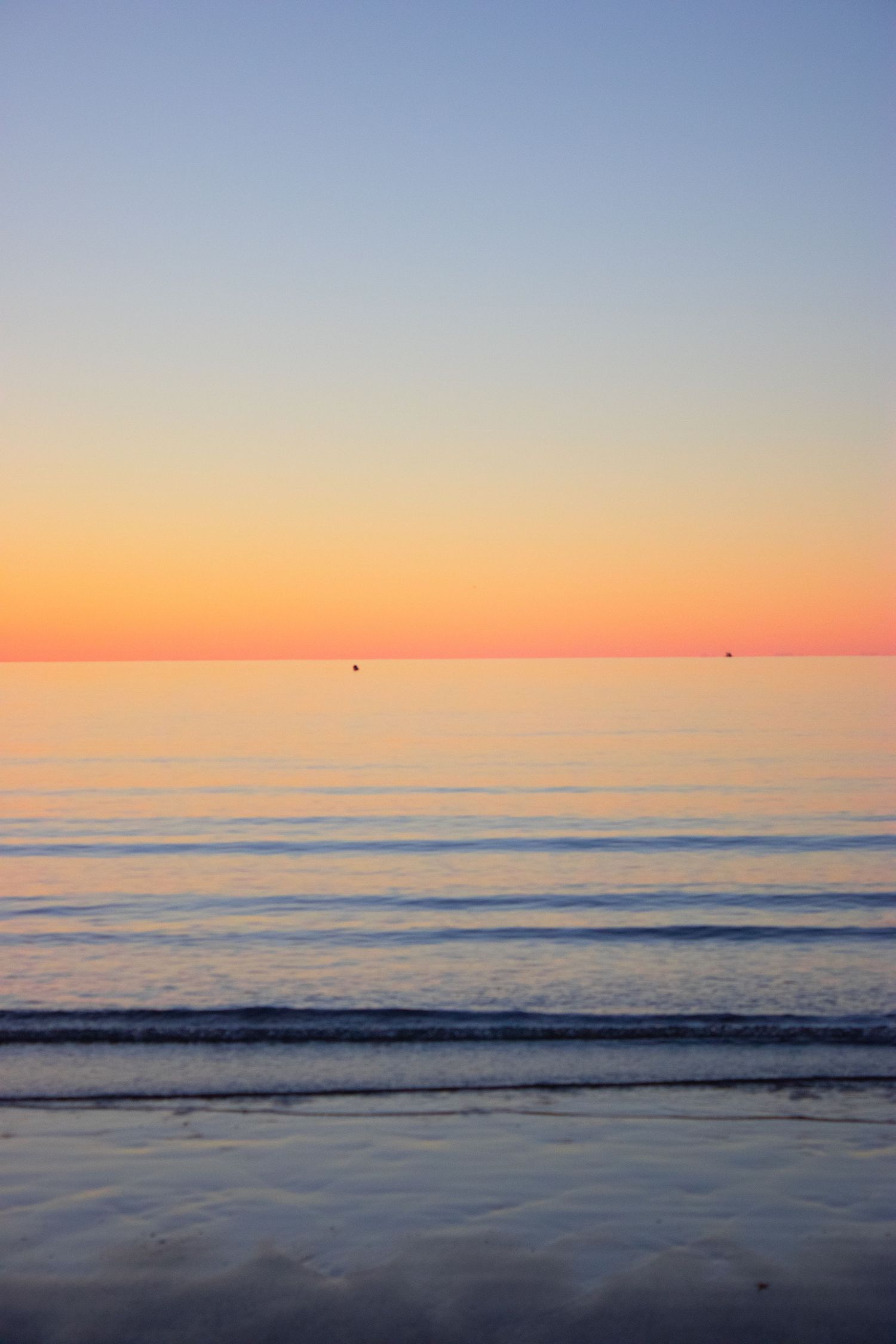 Peaceful ocean sunset with warm orange horizon gradient reflecting on calm shallow waves.