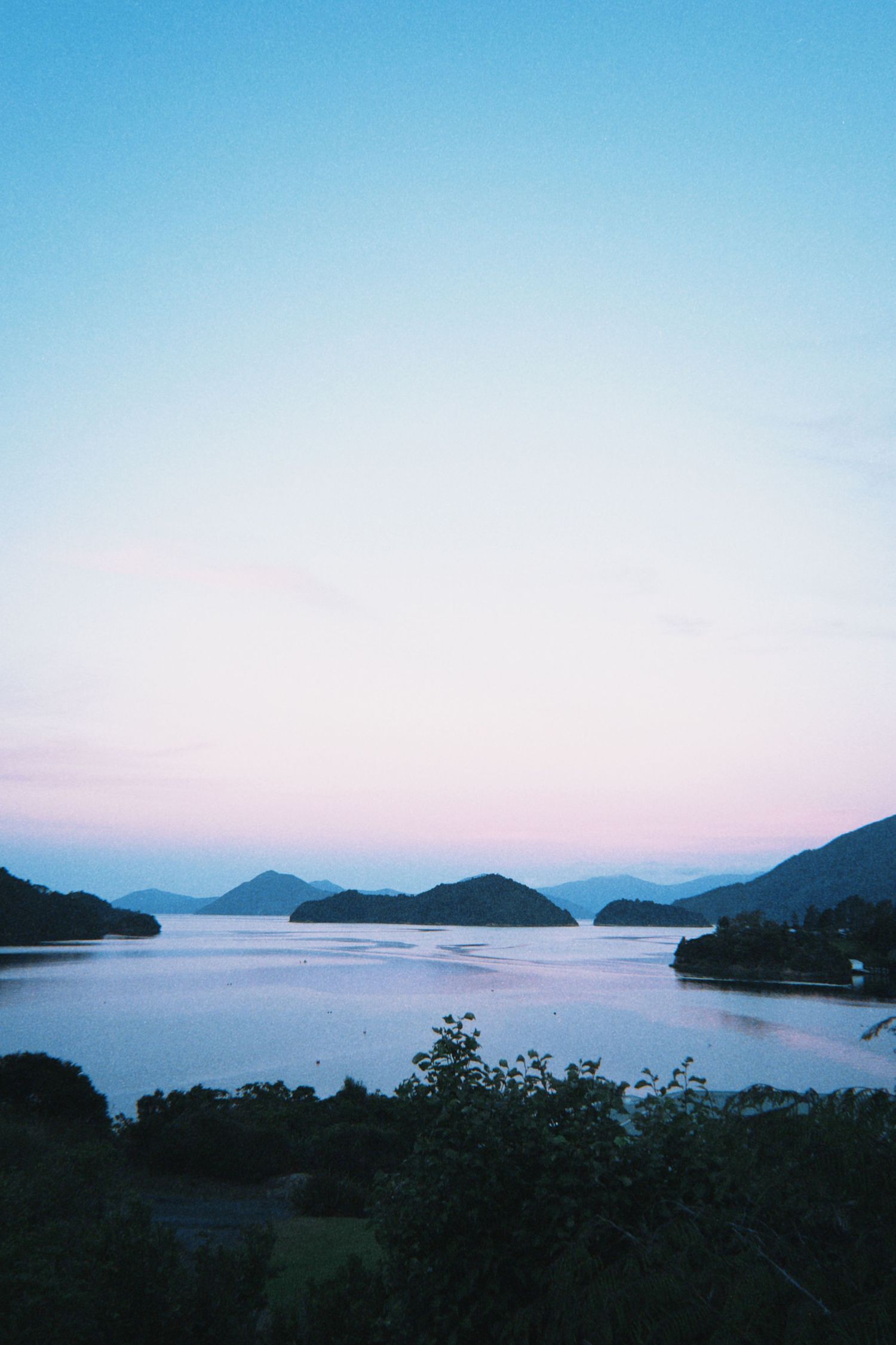 Serene twilight panorama of mountain islands over still water with pink and blue sky.