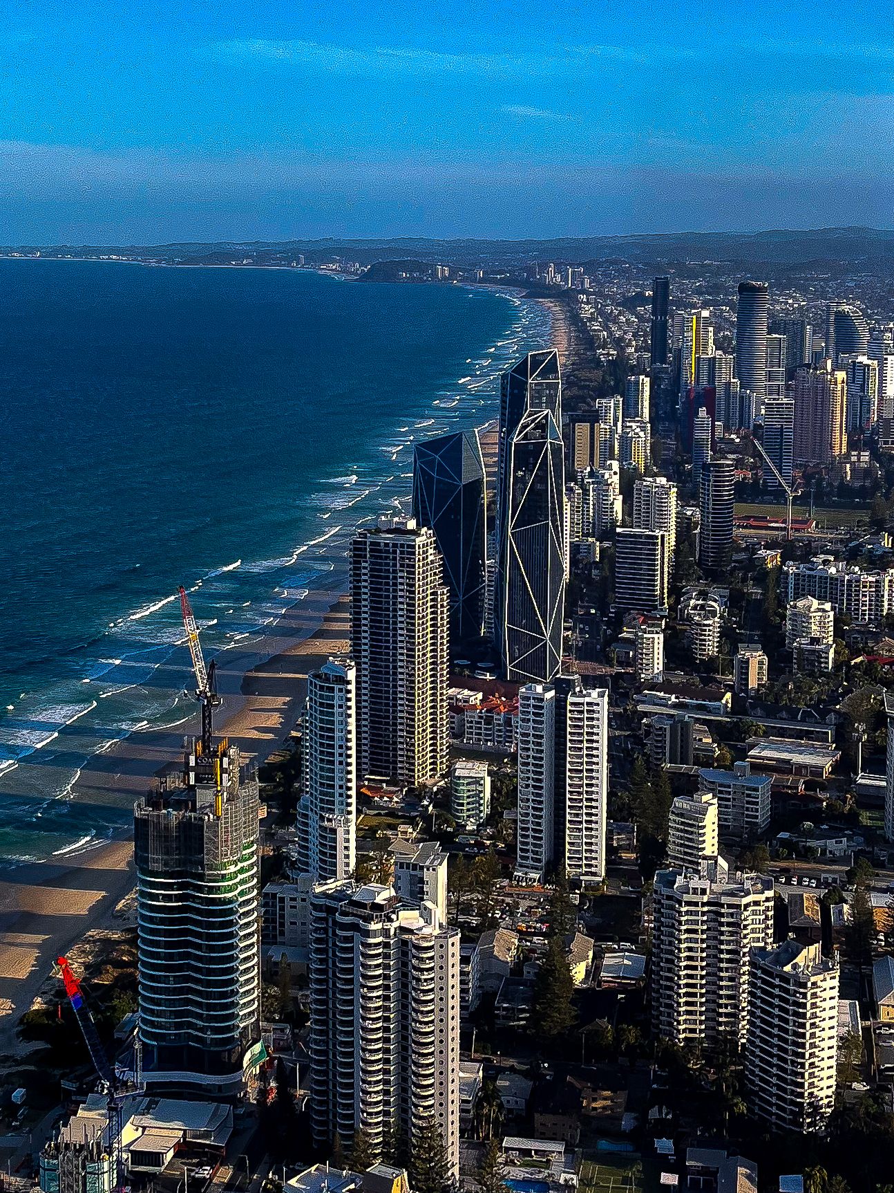 Aerial view of Gold Coast skyline with skyscrapers stretching along sandy ocean beach.