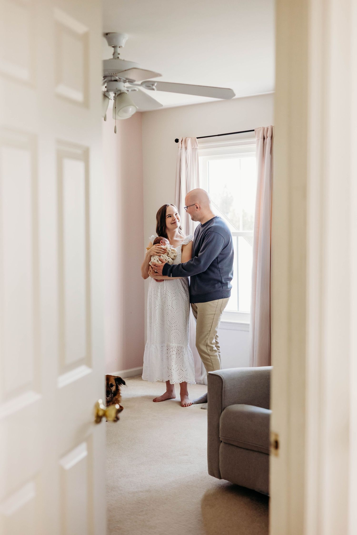 New parents share a tender moment holding their newborn baby in a softly lit nursery room.