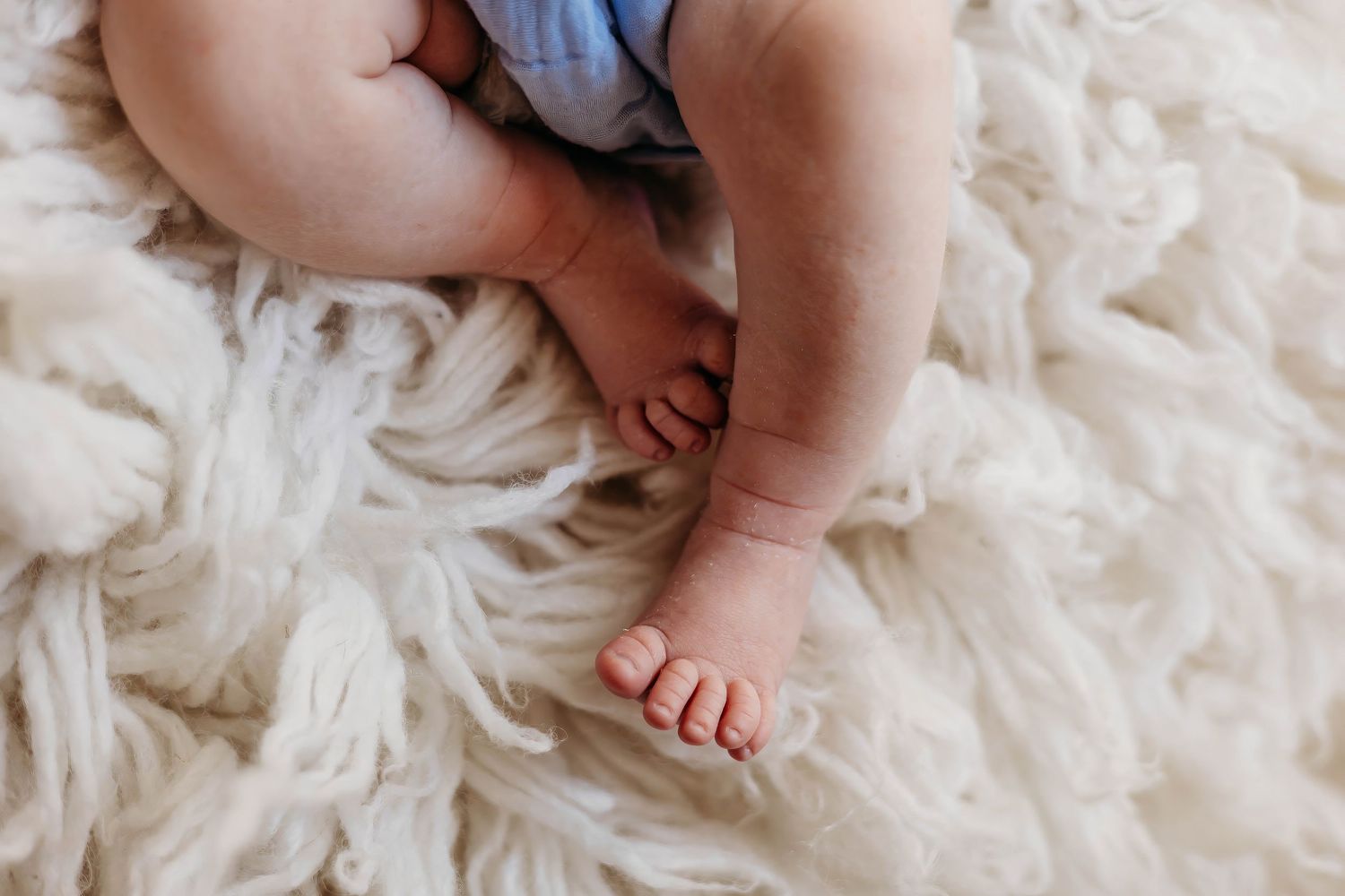 Tiny newborn baby feet resting on a soft white fluffy blanket during a lifestyle newborn photography session.