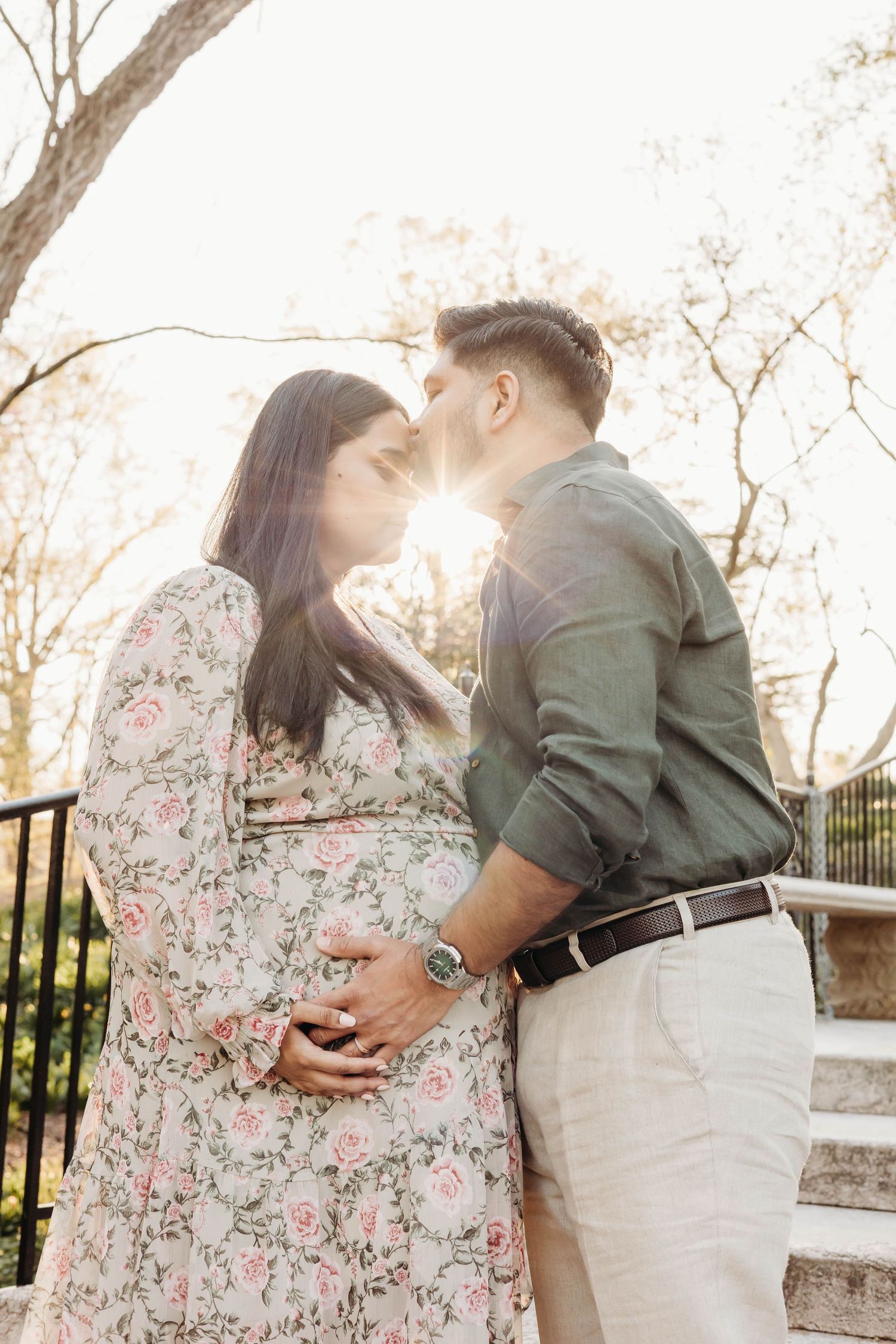 Expecting couple shares a romantic sunset kiss while cradling baby bump during outdoor maternity photos.