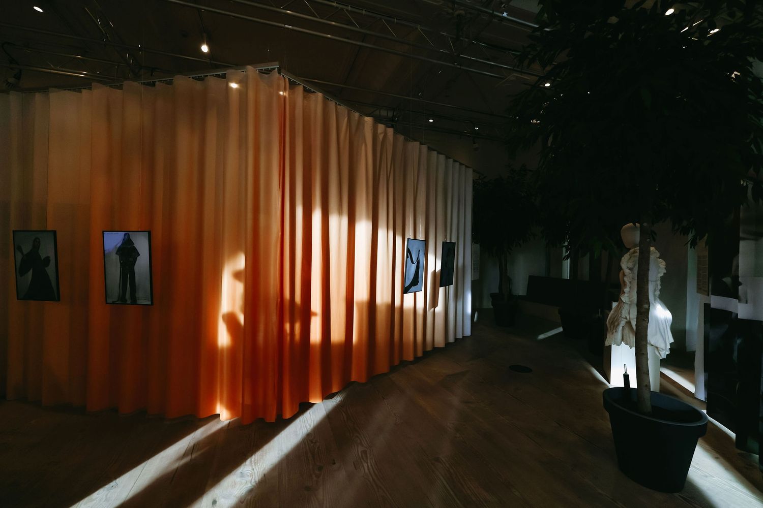 Art gallery exhibition space with orange curtain divider and dramatic lighting creating long shadows.