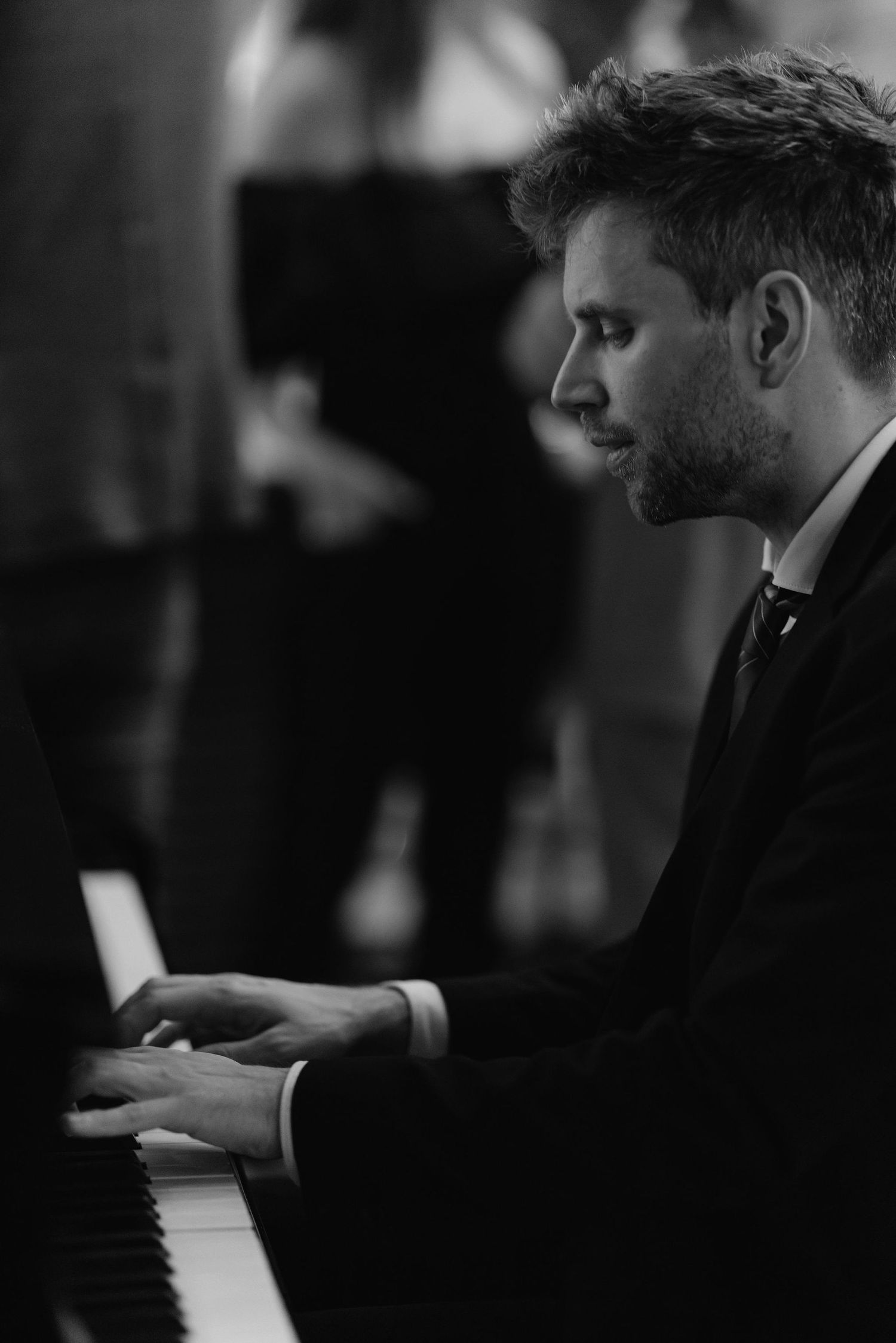 A musician in formal attire plays piano in a dimly lit setting.