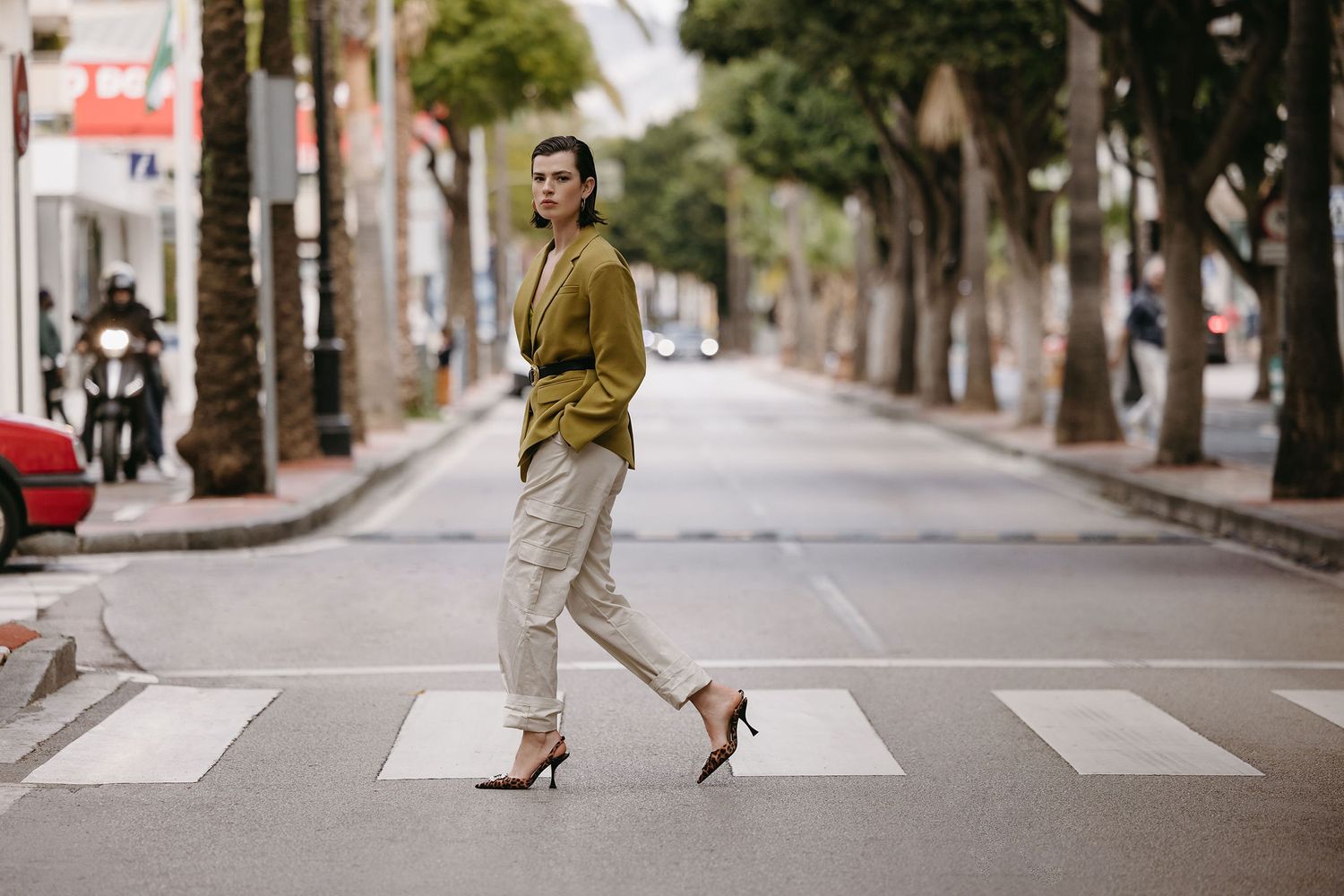 Stylish street fashion shot of person crossing zebra crossing in mustard jacket and heels.