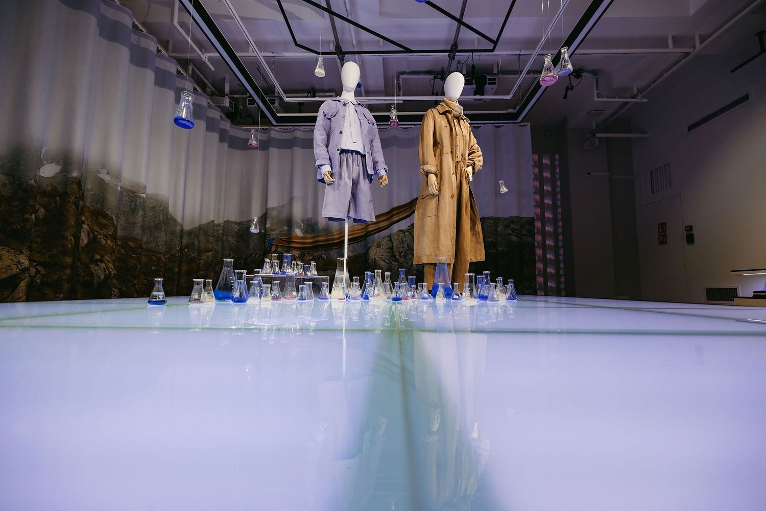Fashion display with floating mannequins wearing coats above blue-lit platform with glass elements.