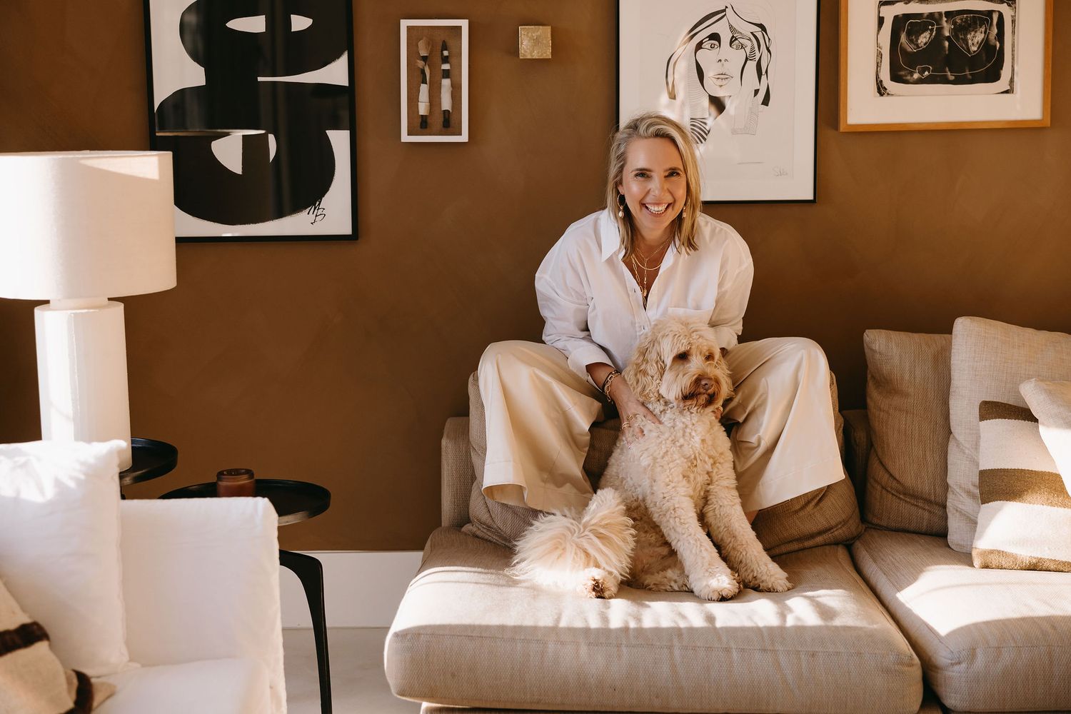 Person sitting on couch with golden retriever dog in modern room with art prints.