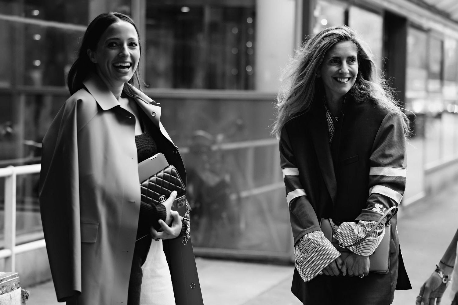 Two people in winter coats posing on city street in monochrome.