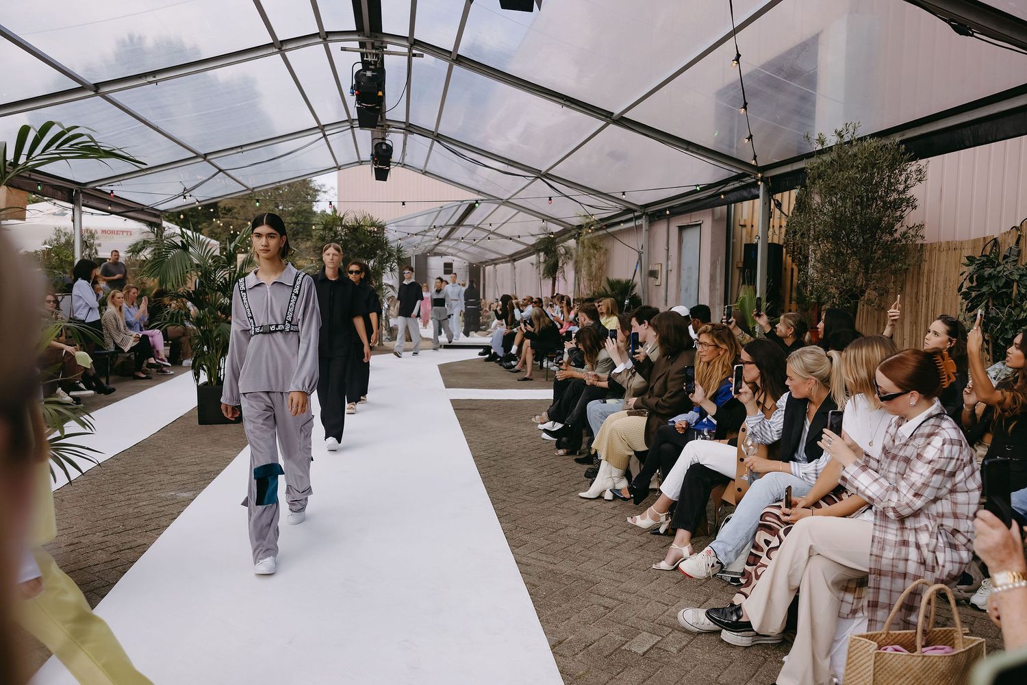 Indoor fashion show with runway and greenhouse-style ceiling.