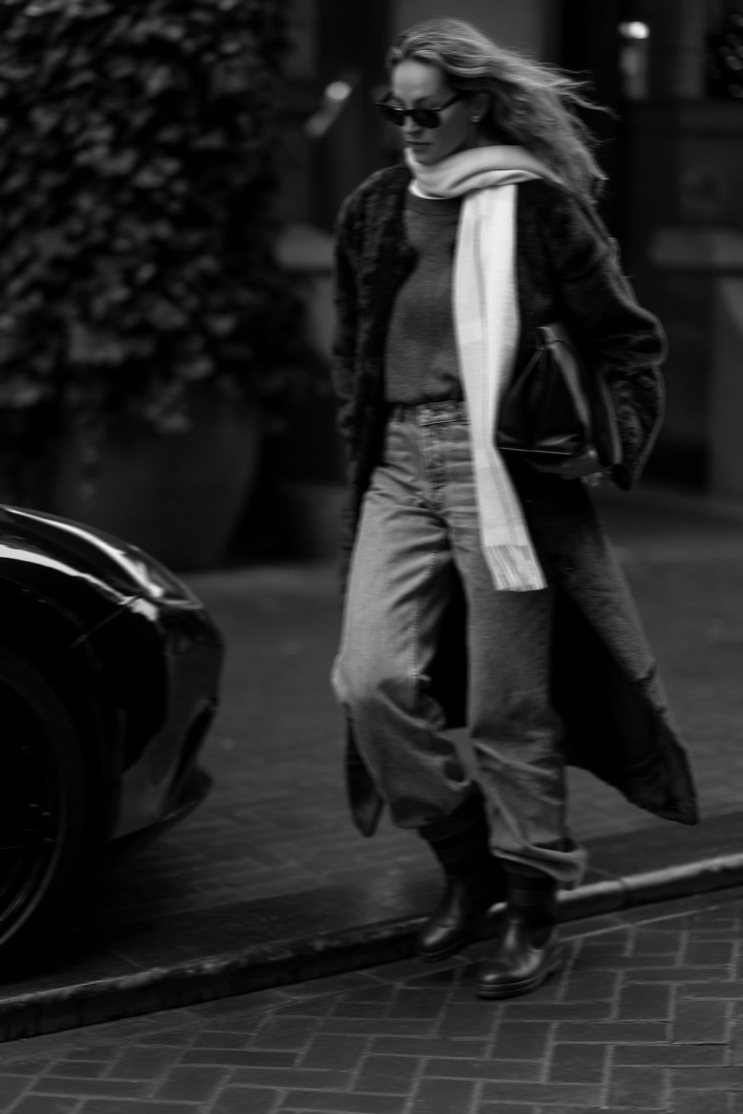 Black and white street style photo with long coat, scarf and jeans in urban setting.