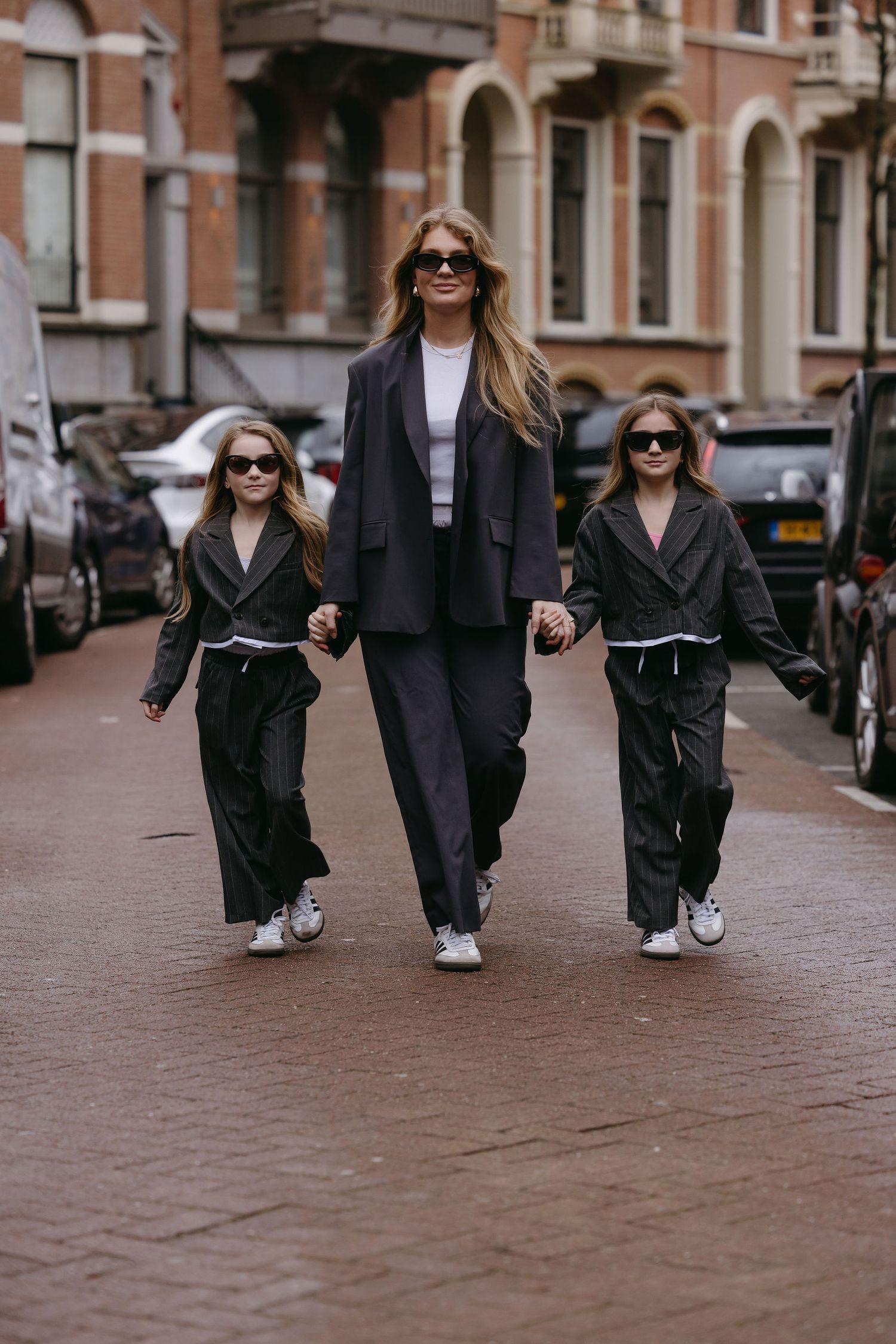 Coordinated family street style featuring matching dark outerwear and sunglasses on brick sidewalk.