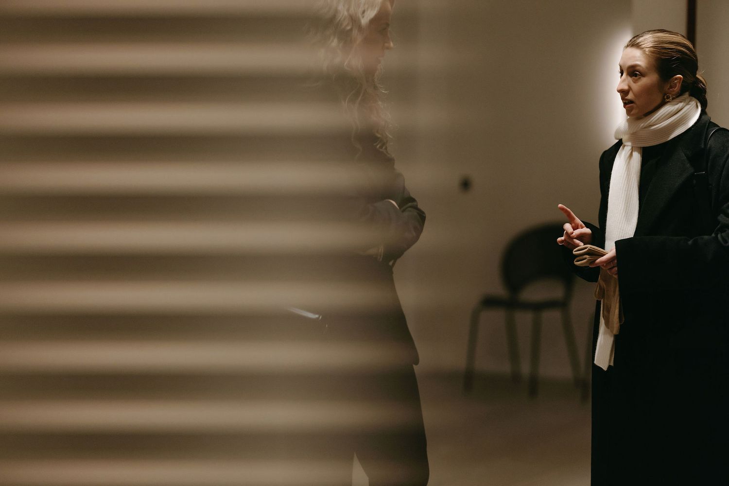 A dramatic side-lit silhouette of a figure in formal attire speaking in a dark interior space.