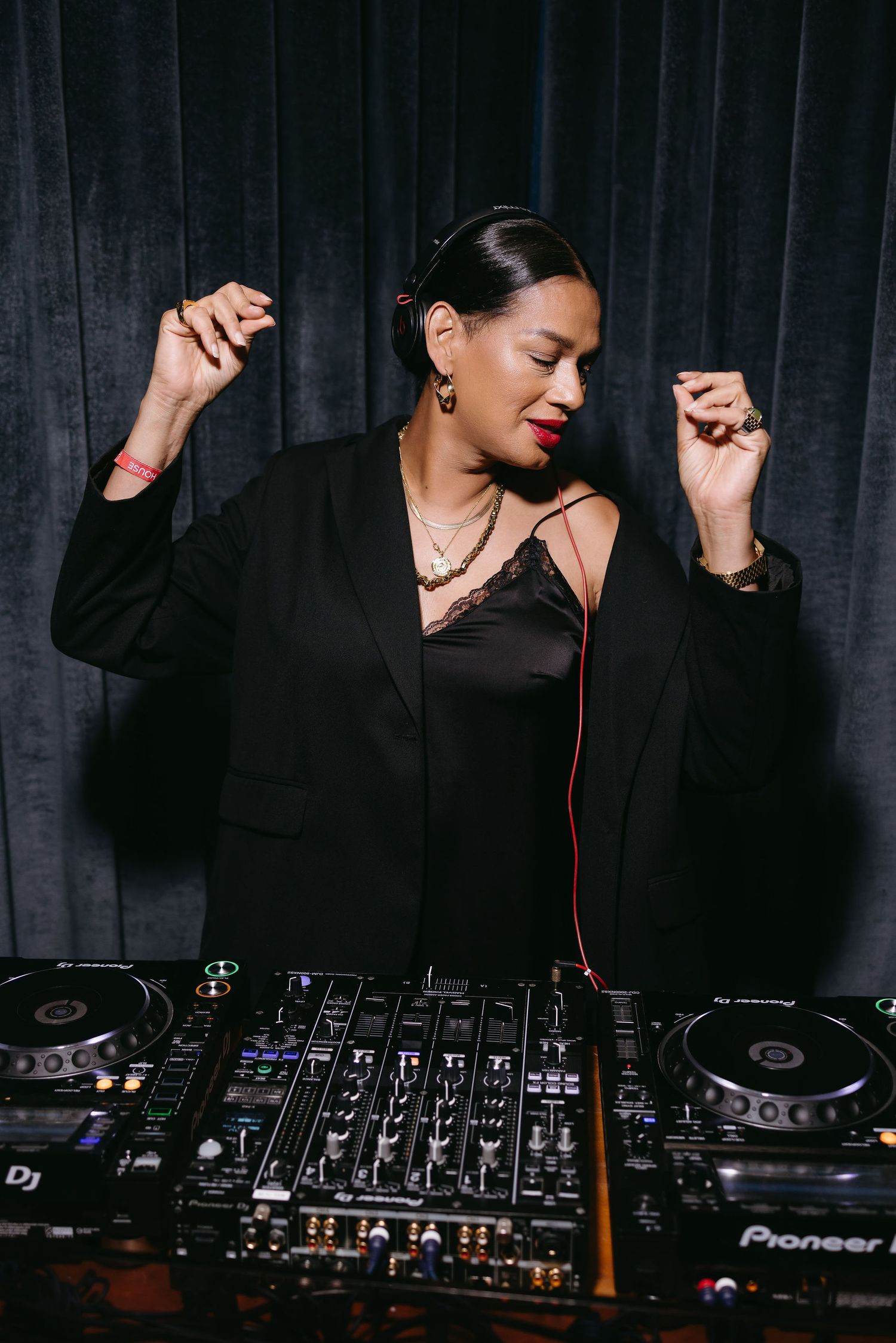 DJ performing with Pioneer equipment against dark backdrop wearing black outfit.
