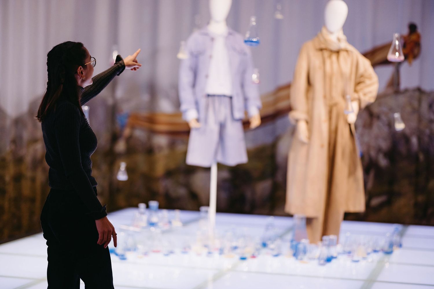 Exhibition setup showing mannequins displaying fashion pieces with dramatic lighting and scattered confetti.