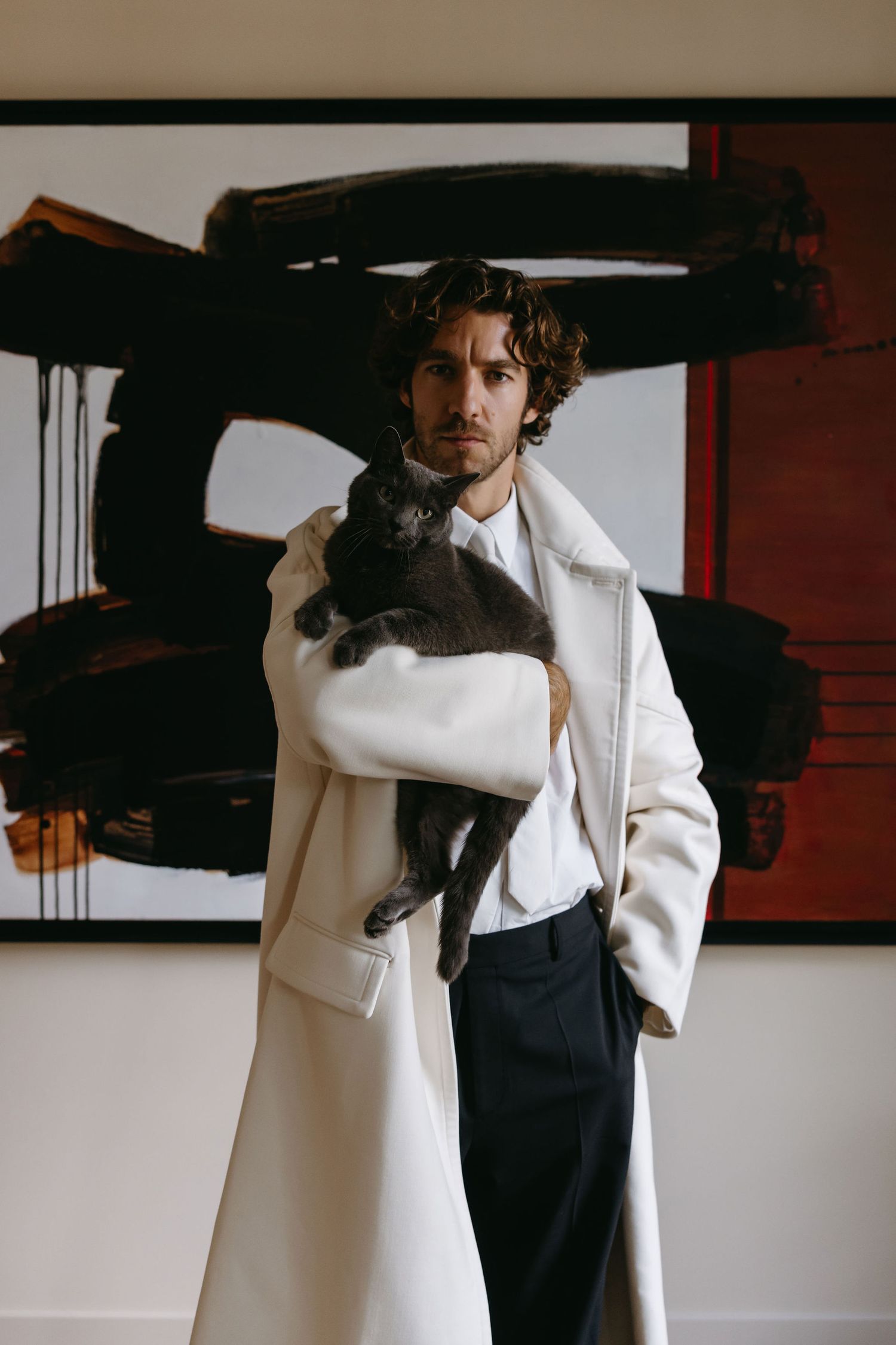 Stylish portrait of someone wearing a white coat with black trousers against an abstract art background.