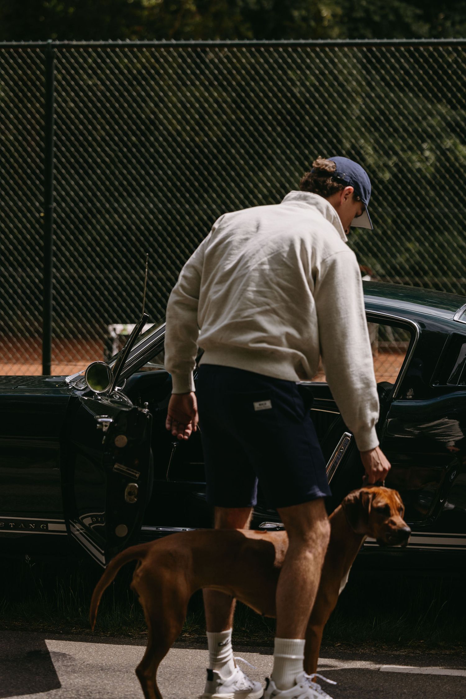 Person in casual wear walking dog beside vintage car.