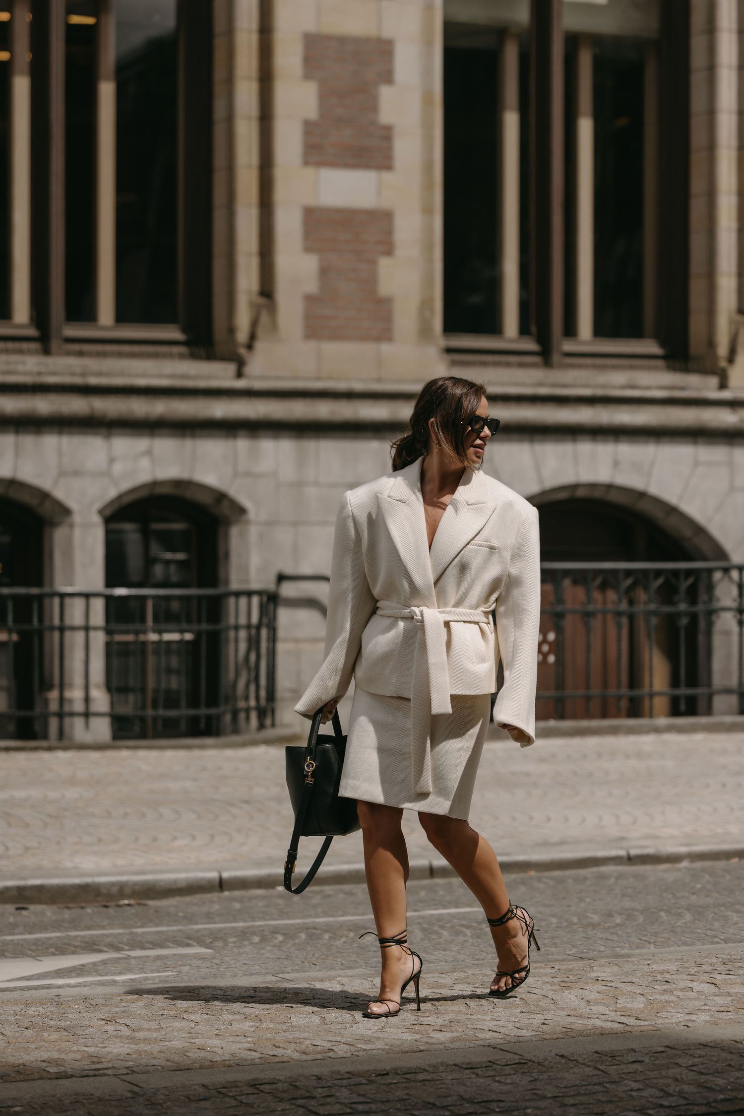 Elegant white belted suit ensemble paired with heels on cobblestone street.