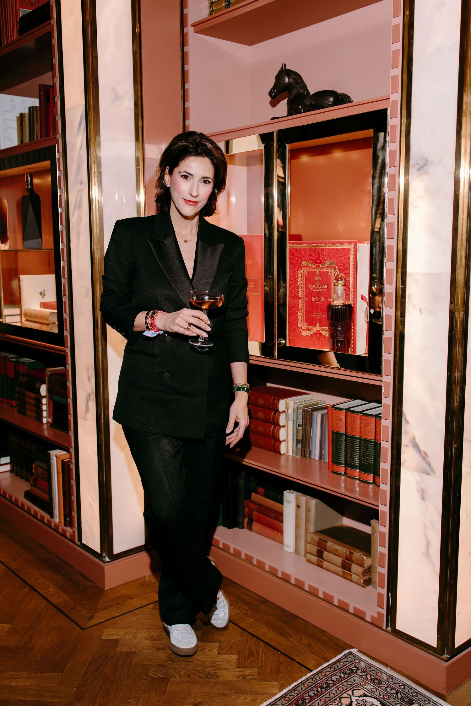 Stylish black pantsuit ensemble photographed against wooden bookshelves with decorative accents.