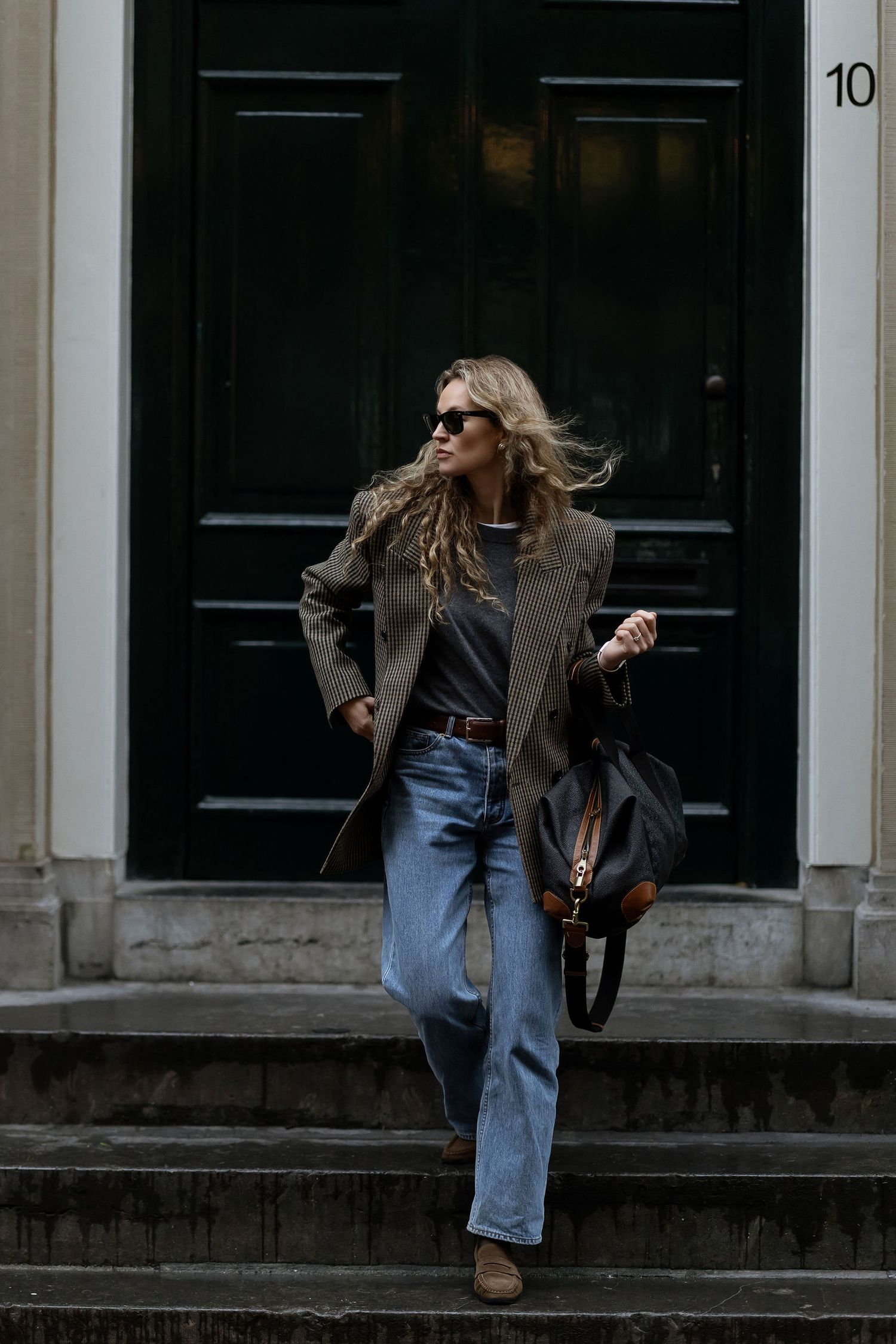 A person in denim and leather spins and dances dramatically on a city sidewalk in front of dark doorways.