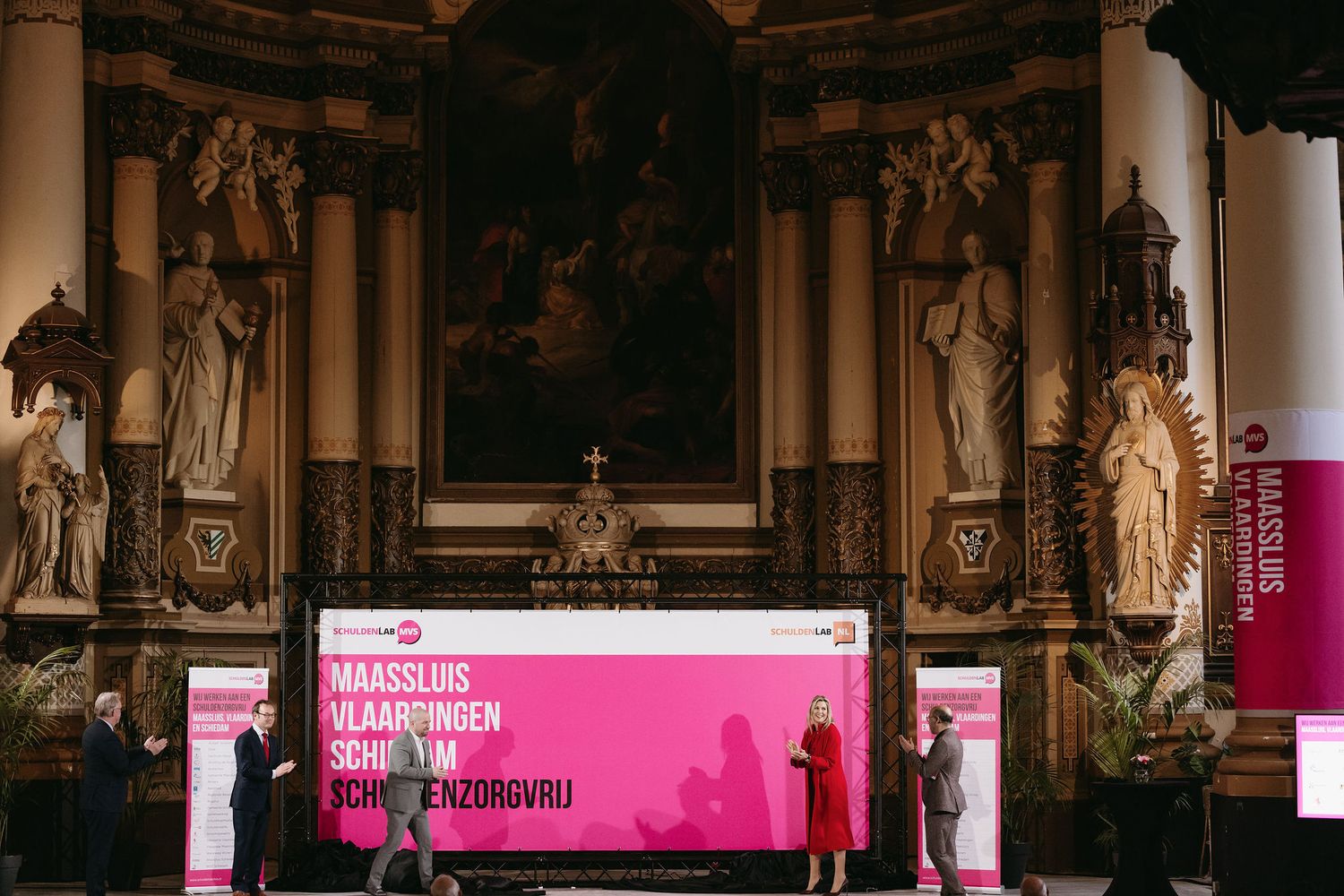 An ornate church interior with classical statues and a pink-lit stage setup for a modern presentation.