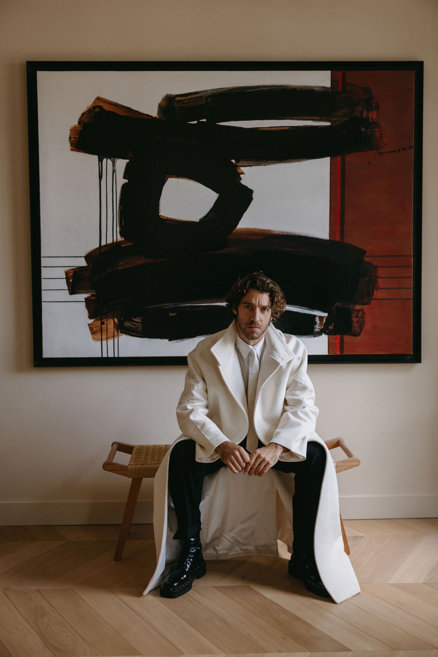 Modern fashion portrait with white suit against dramatic black abstract artwork.