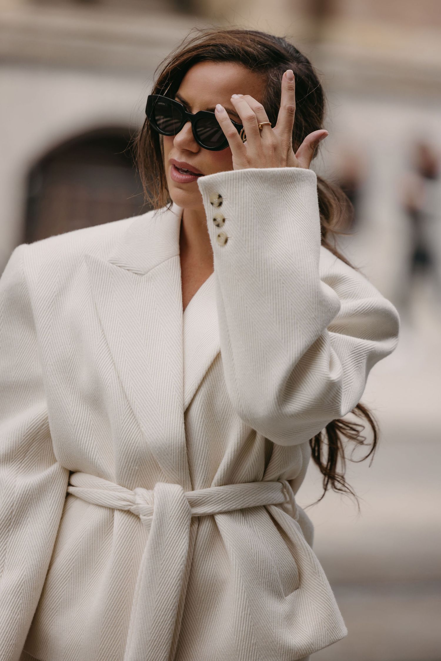 Stylish person wearing an oversized white wool coat with dramatic collar and sunglasses on a city street.