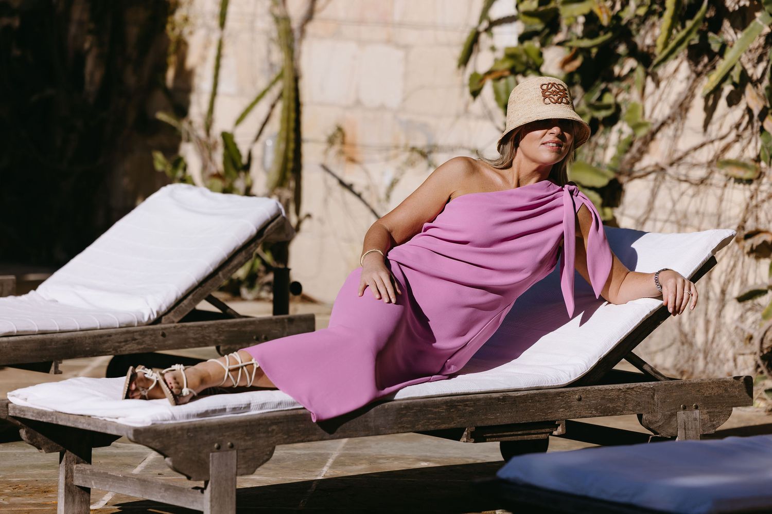 Relaxed summer scene with person lounging in flowing pink dress on outdoor chaise lounge.