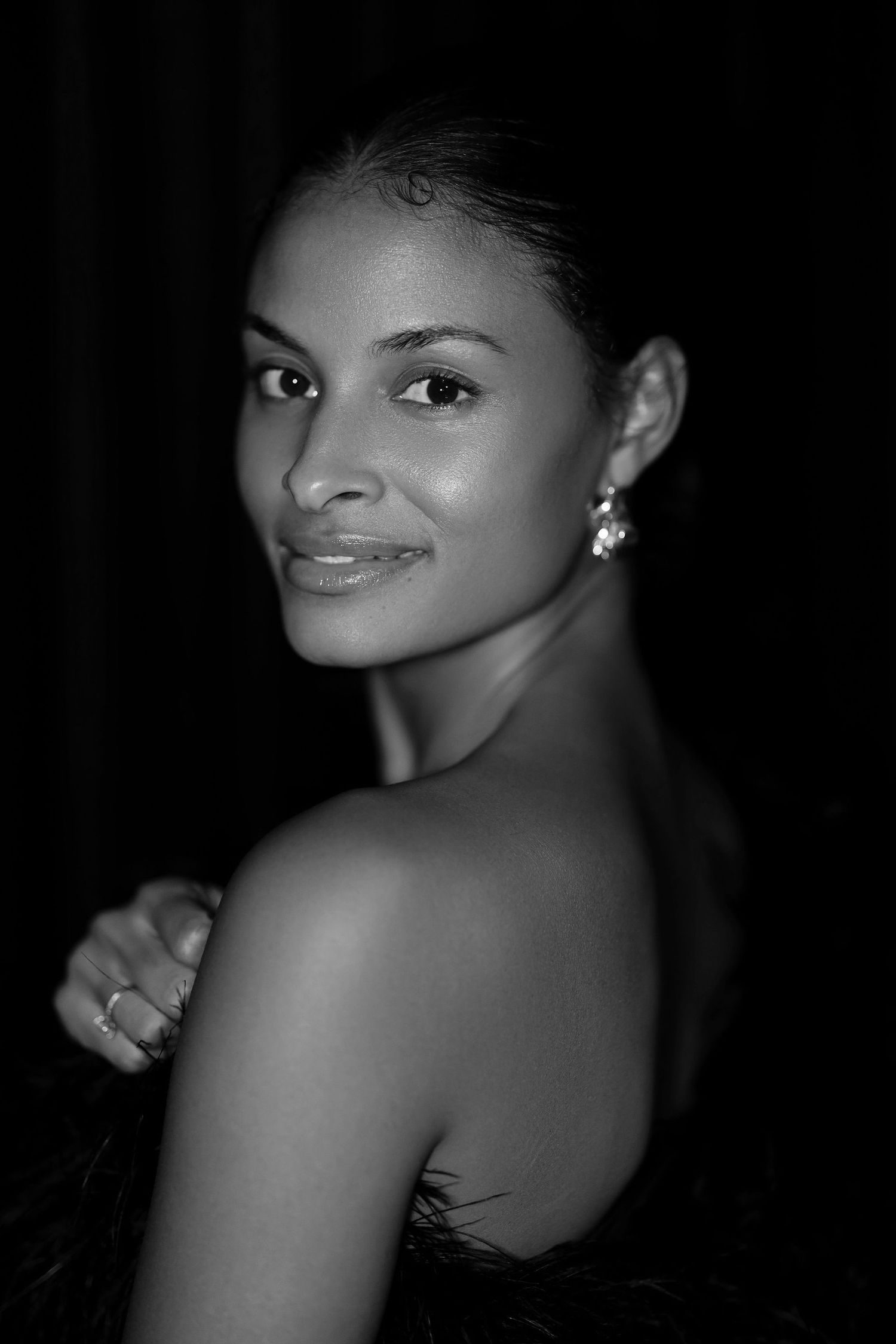 Black and white portrait showing bare shoulder and elegant earring against dark background.