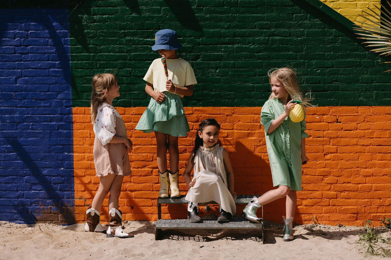 Group of children in pastel outfits posing against colorful geometric painted wall.