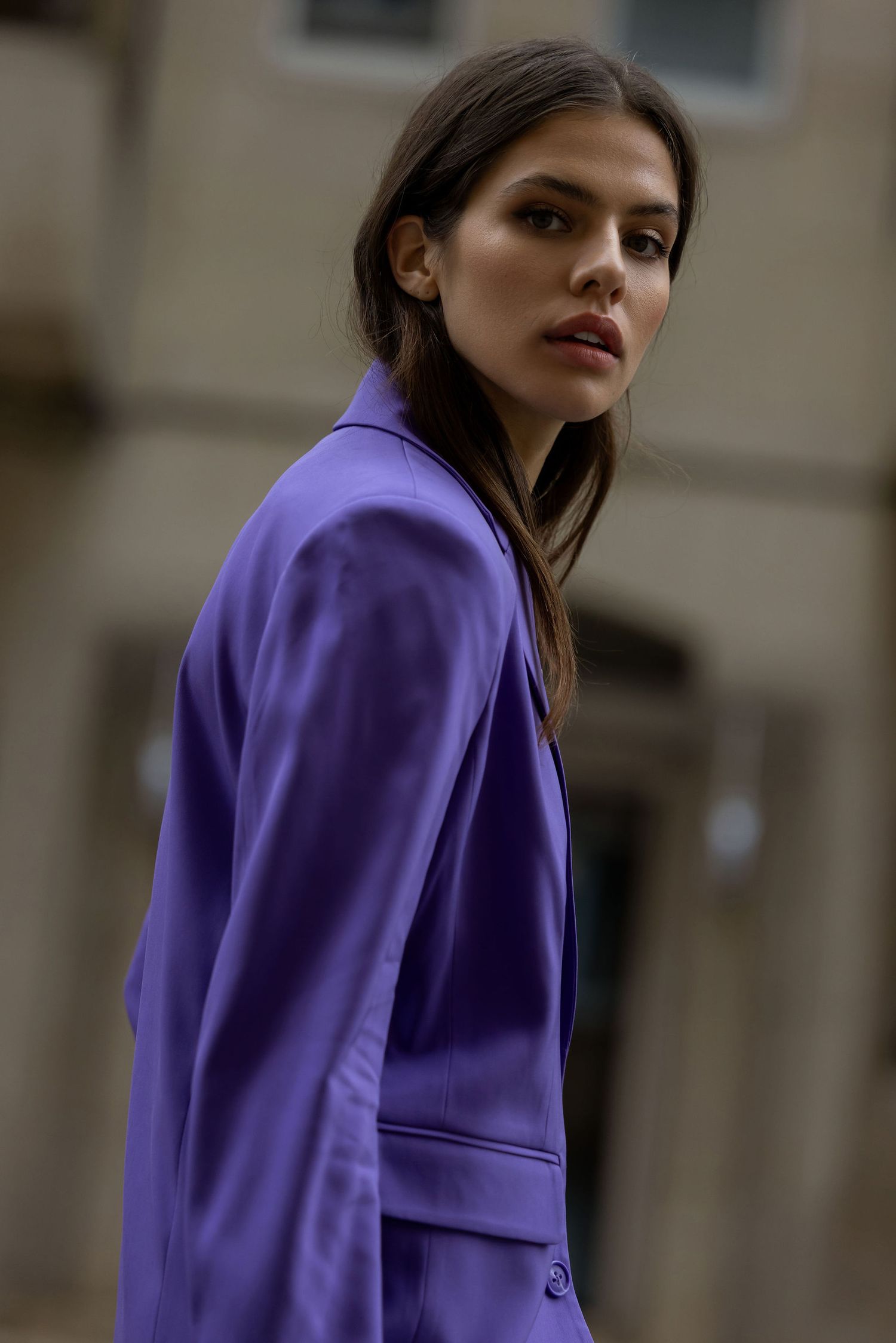 Fashion portrait featuring striking purple blazer against urban architecture backdrop.