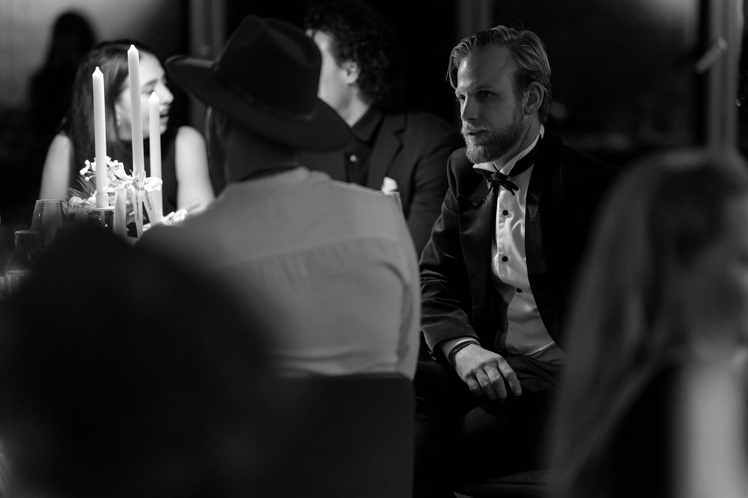 A candid black and white photo capturing conversation at an elegant dinner party.