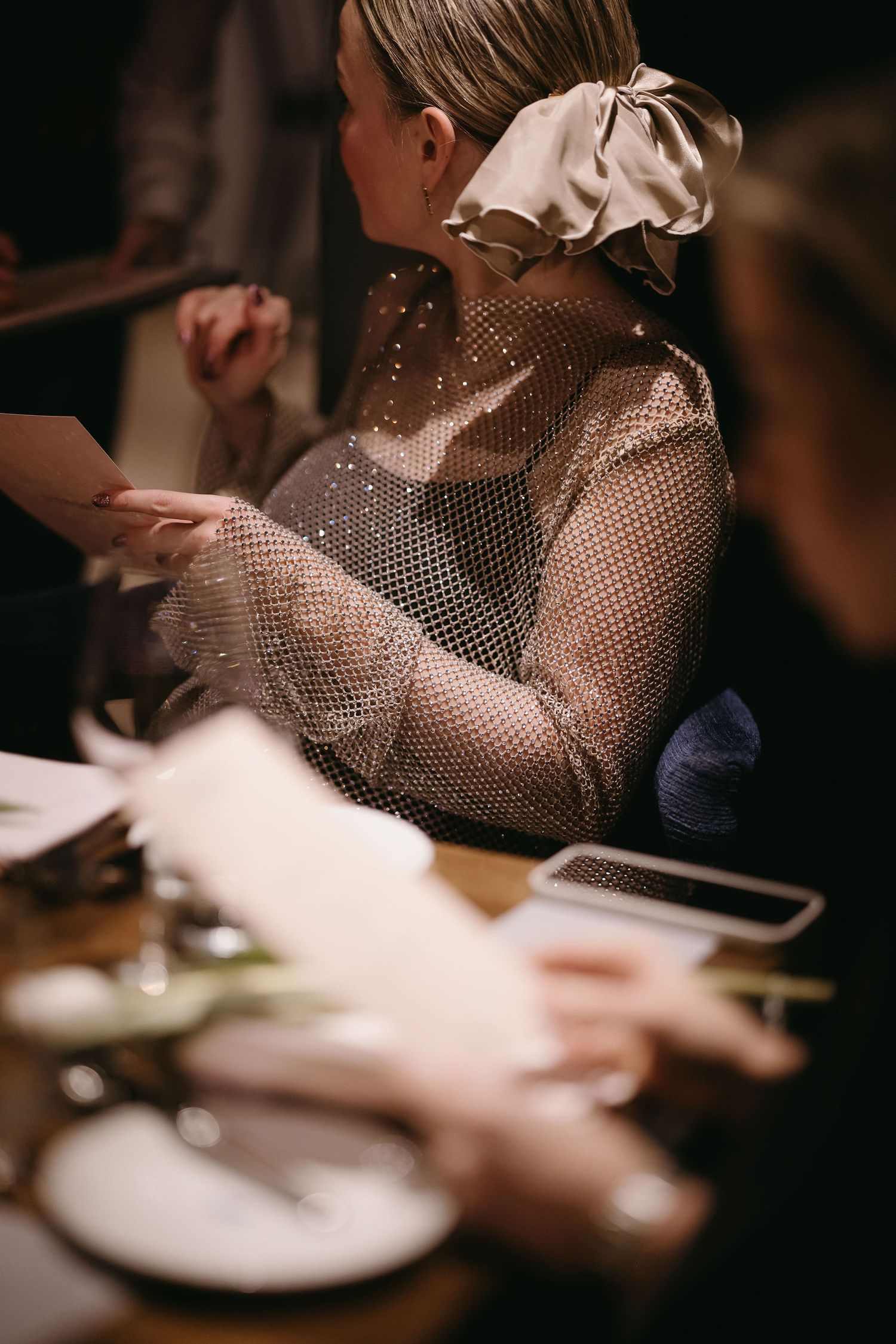 Person wearing sheer sparkly top with bow detail seated at dining table.
