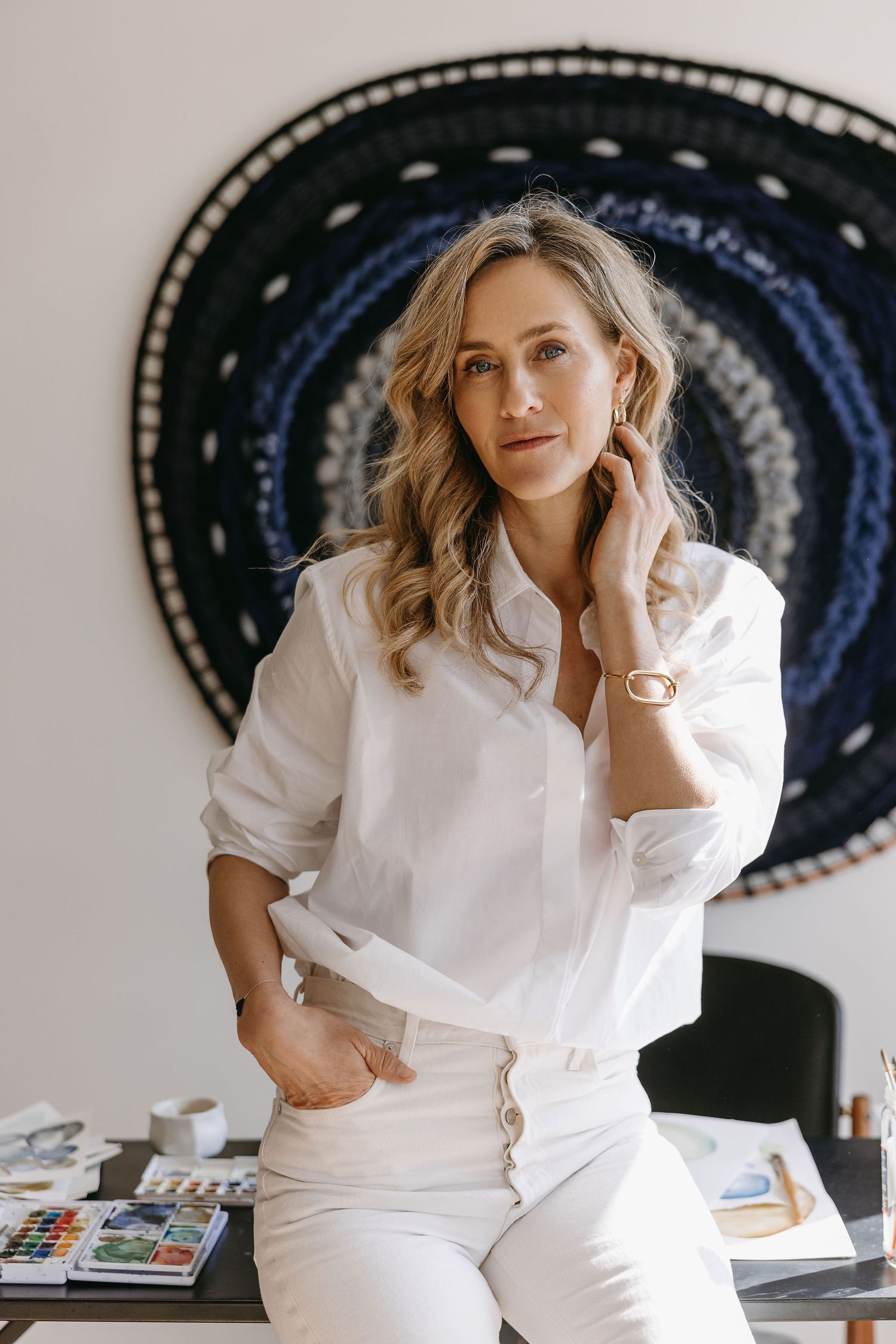 Professional portrait in all-white outfit against dark circular wall art background.