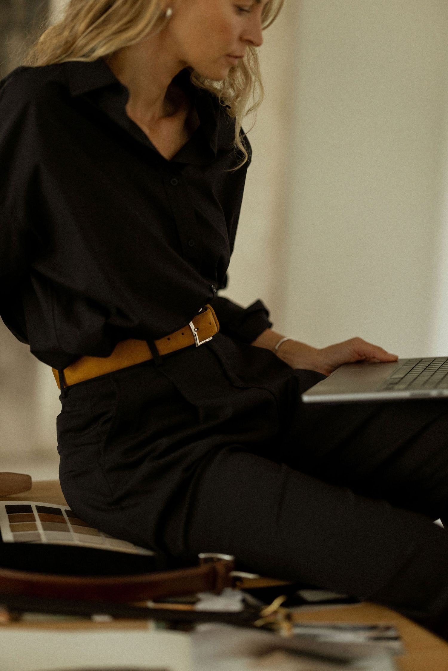 Woman in black outfit working on laptop with guitar in foreground.