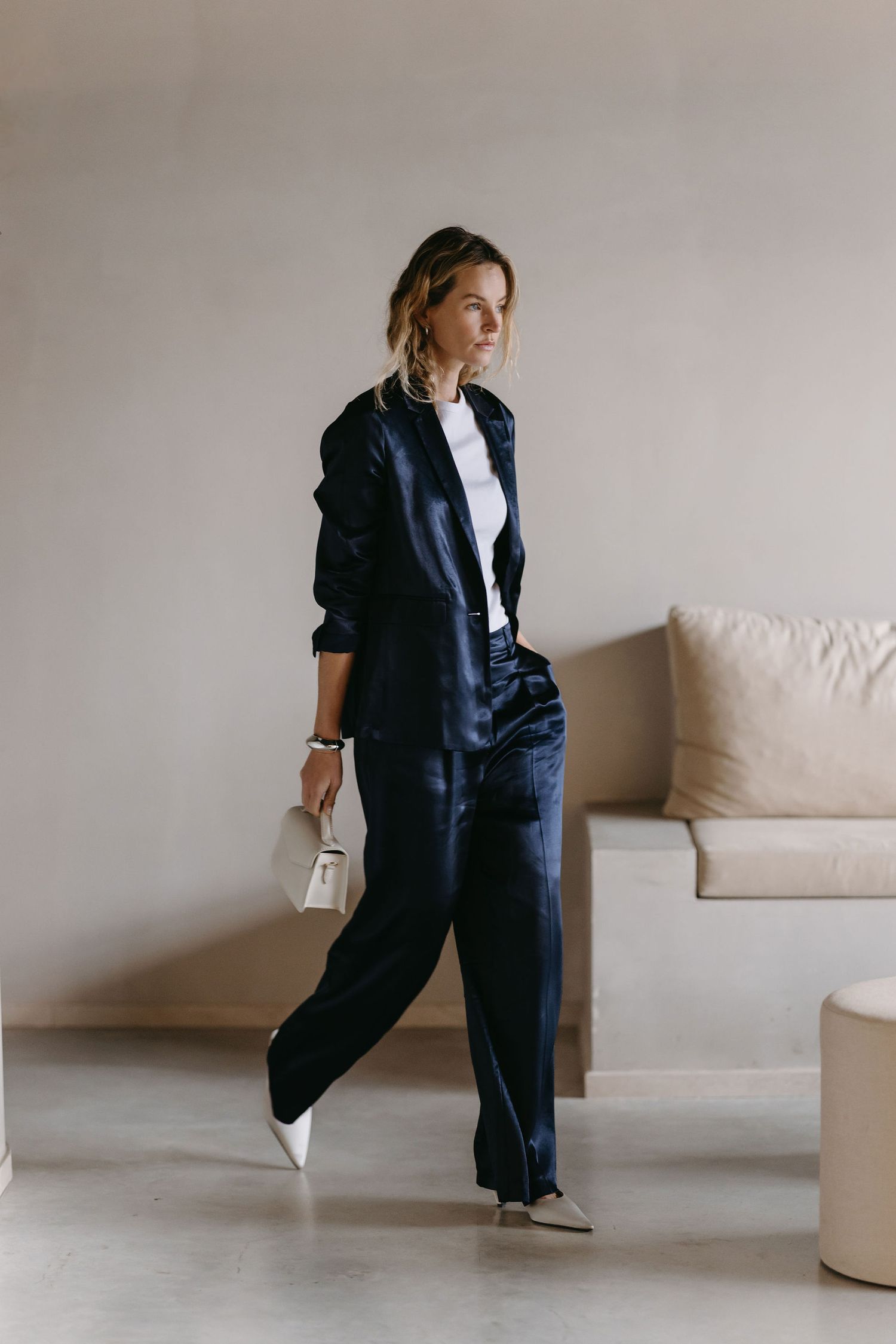 Minimal fashion portrait featuring navy jumpsuit and white sneakers in modern interior setting.