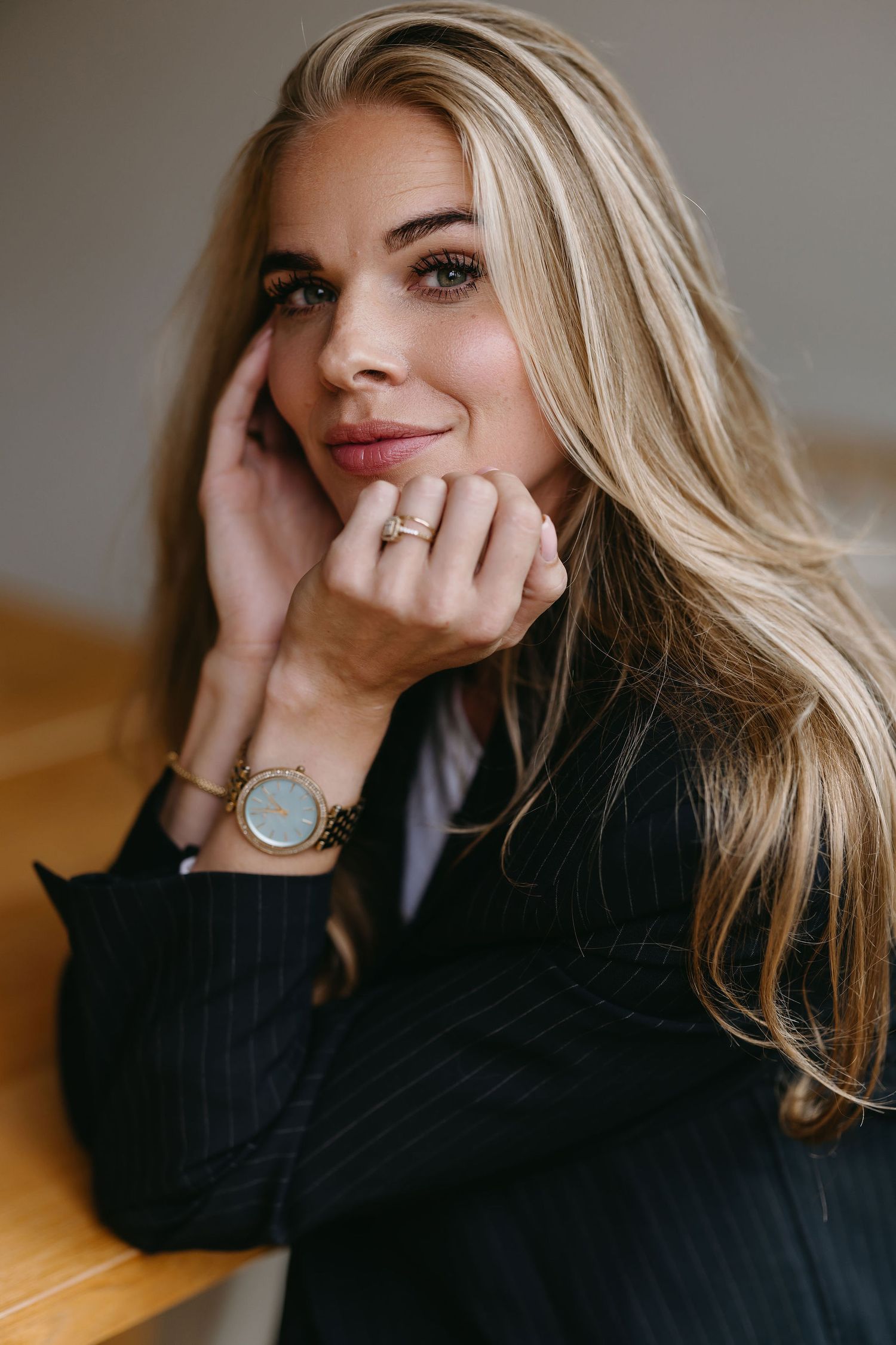 Professional fashion portrait of woman in black sweater with blonde hair and watch resting hand on face.